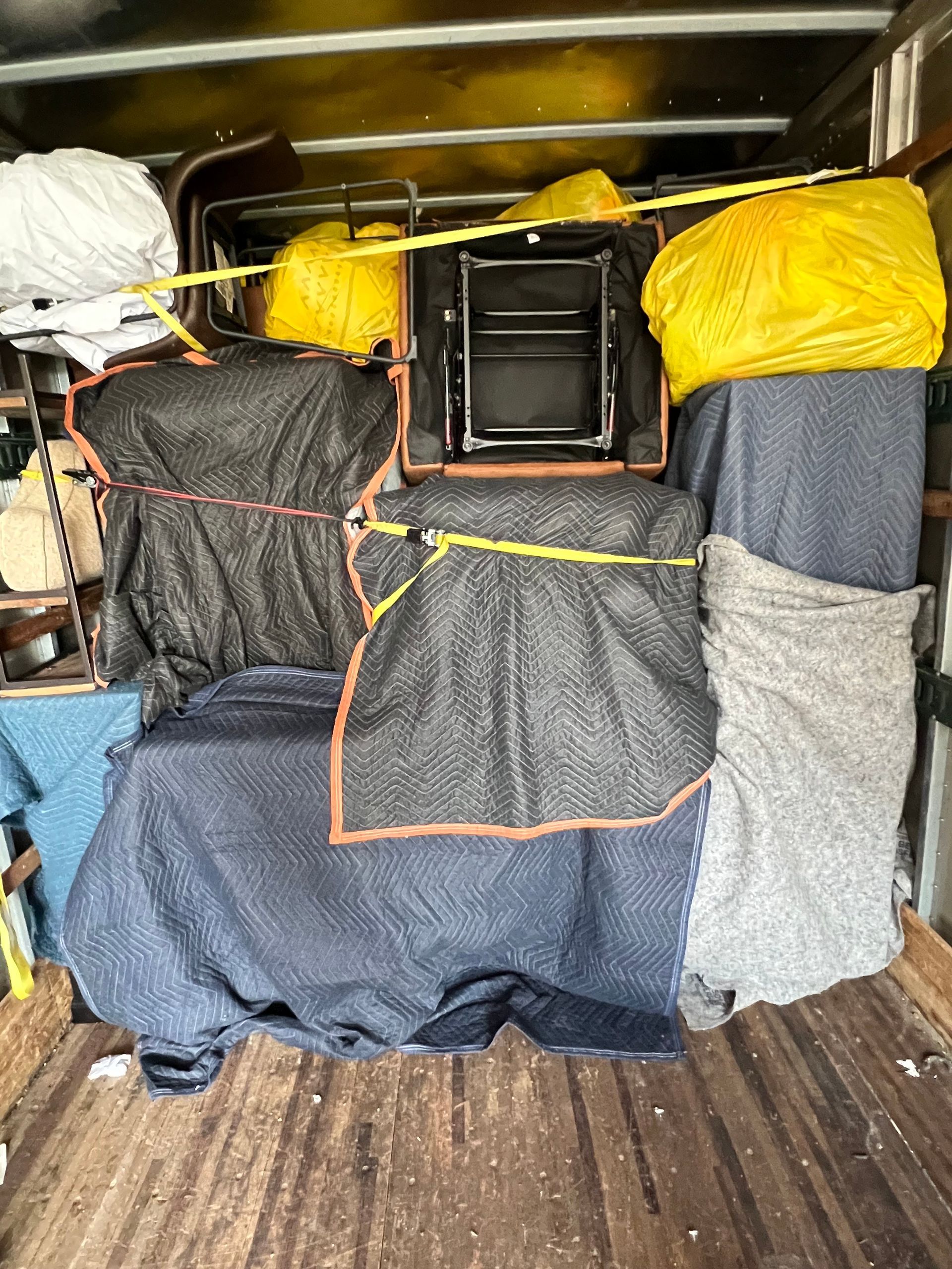 Furniture wrapped in moving blankets secured with yellow tape inside a truck.