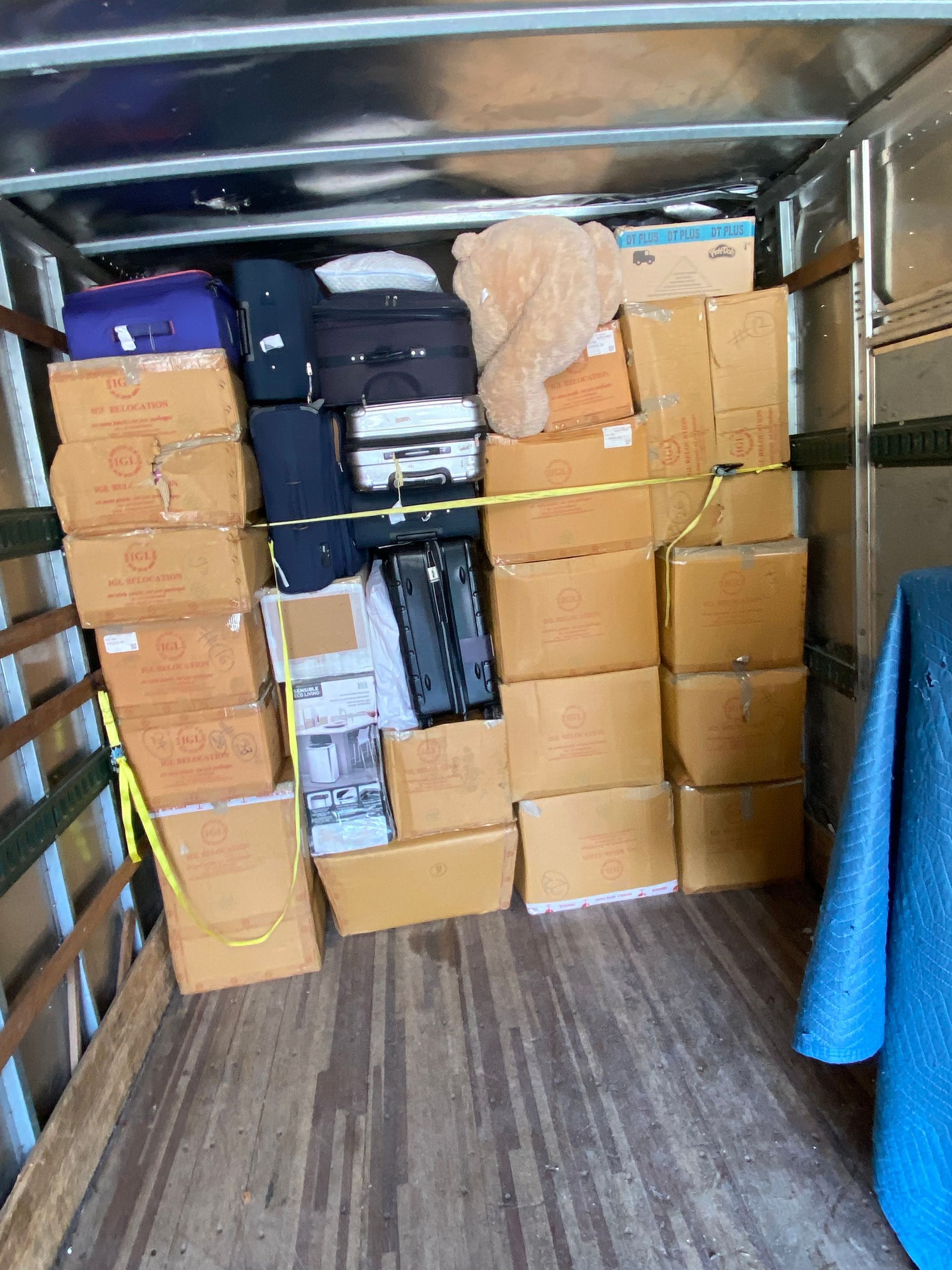 Boxes and luggage packed inside a truck, secured with yellow straps. Brown boxes, black and blue luggage.