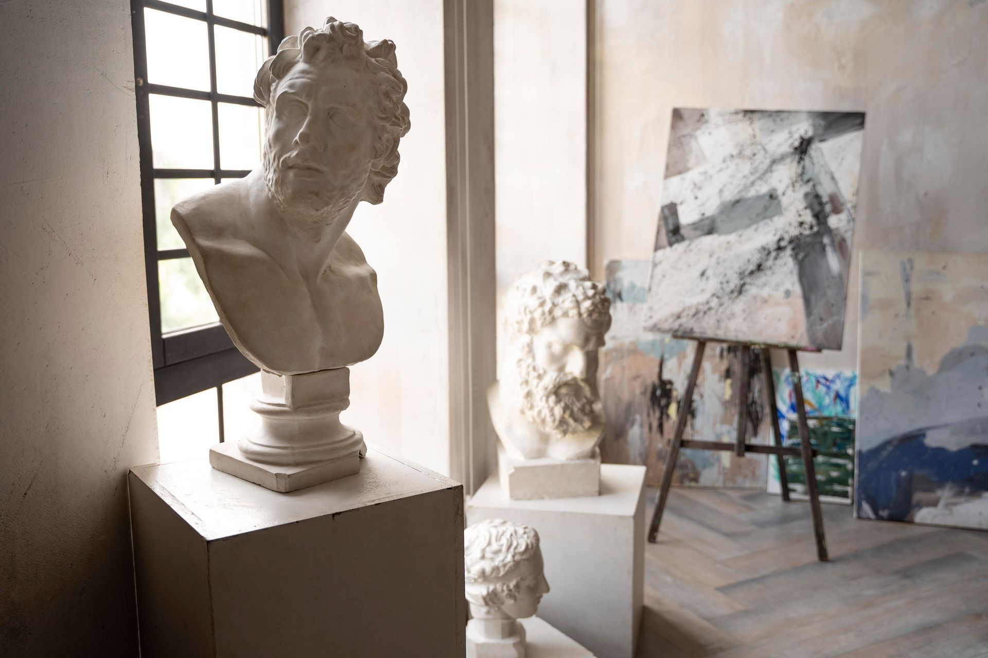 Sculpture studio with busts, easel with painting, and natural light from a window.
