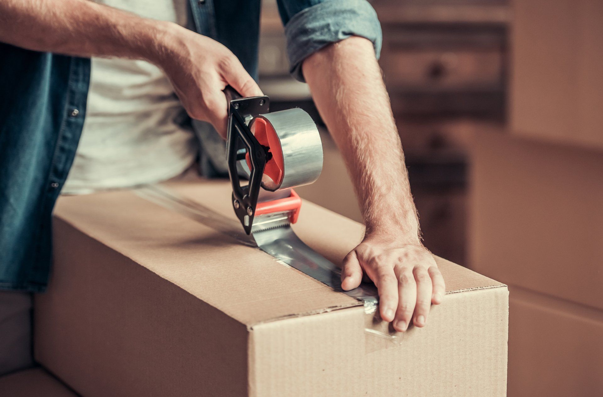 Person taping a cardboard box shut with a tape gun in preparation for moving.