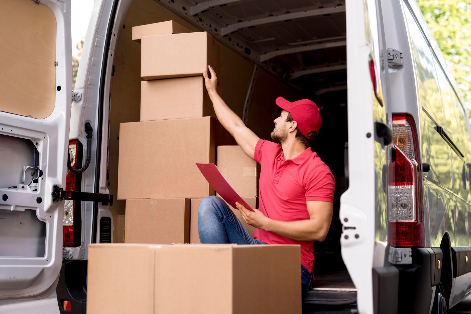 Delivery person in red shirt and cap, sorting boxes in a van.