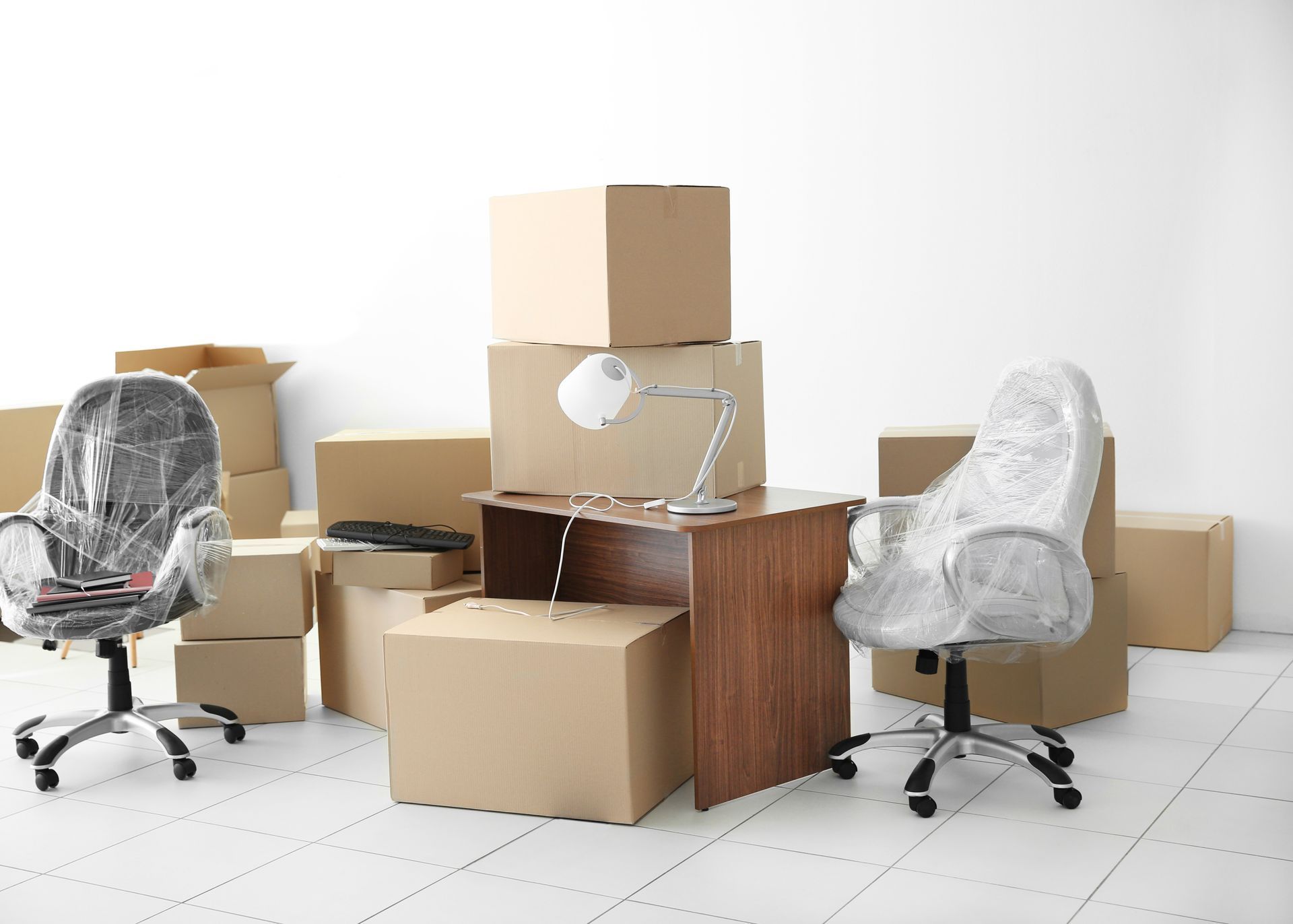 Office space being packed up. Boxes, desk, and chairs covered in plastic.