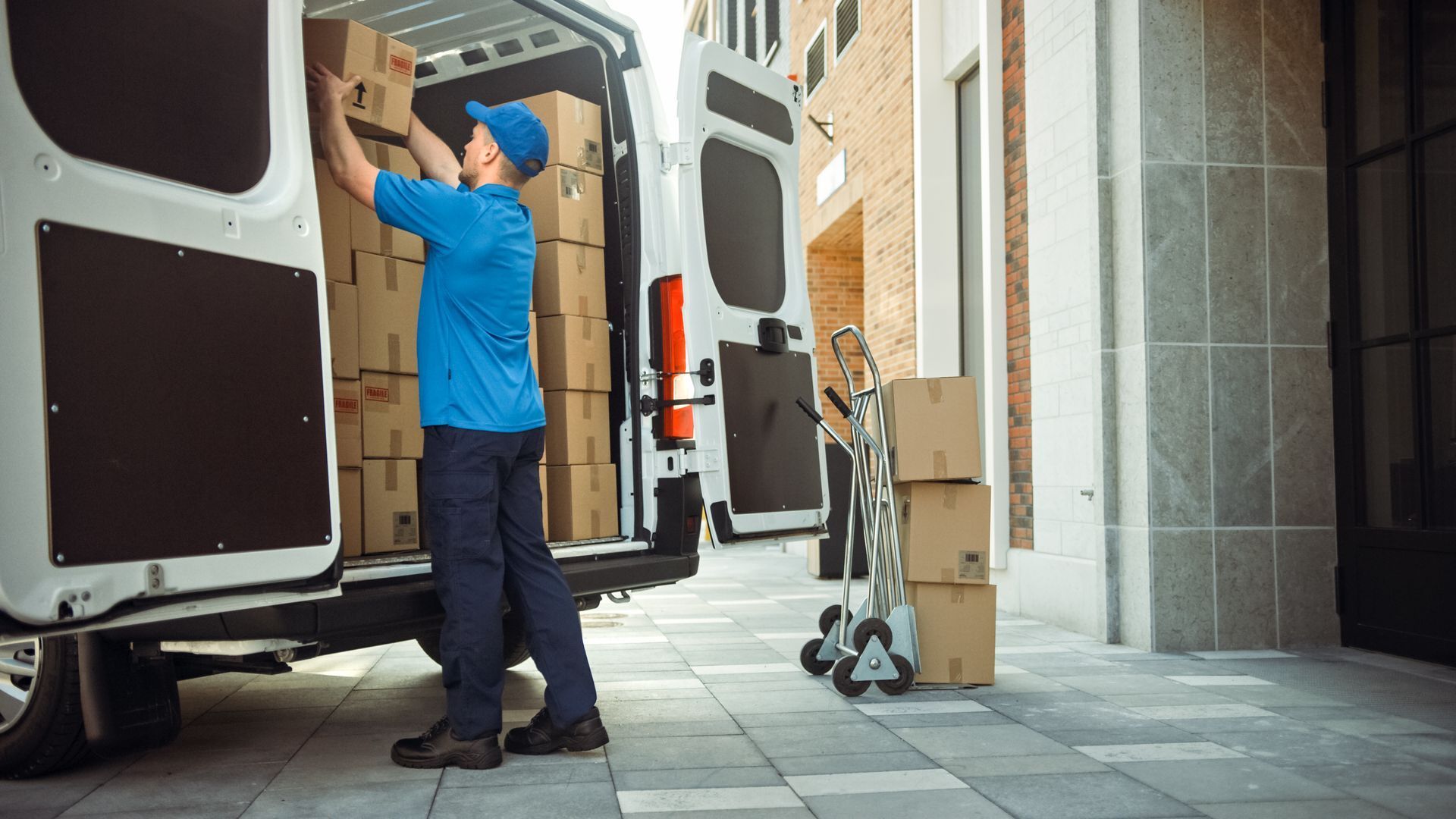 Delivery person loading boxes into a van, standing outside a building.