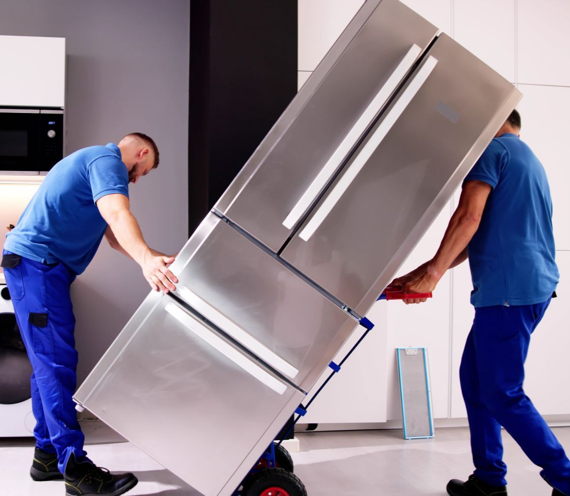Two movers in blue uniforms lifting a stainless steel refrigerator in a kitchen.