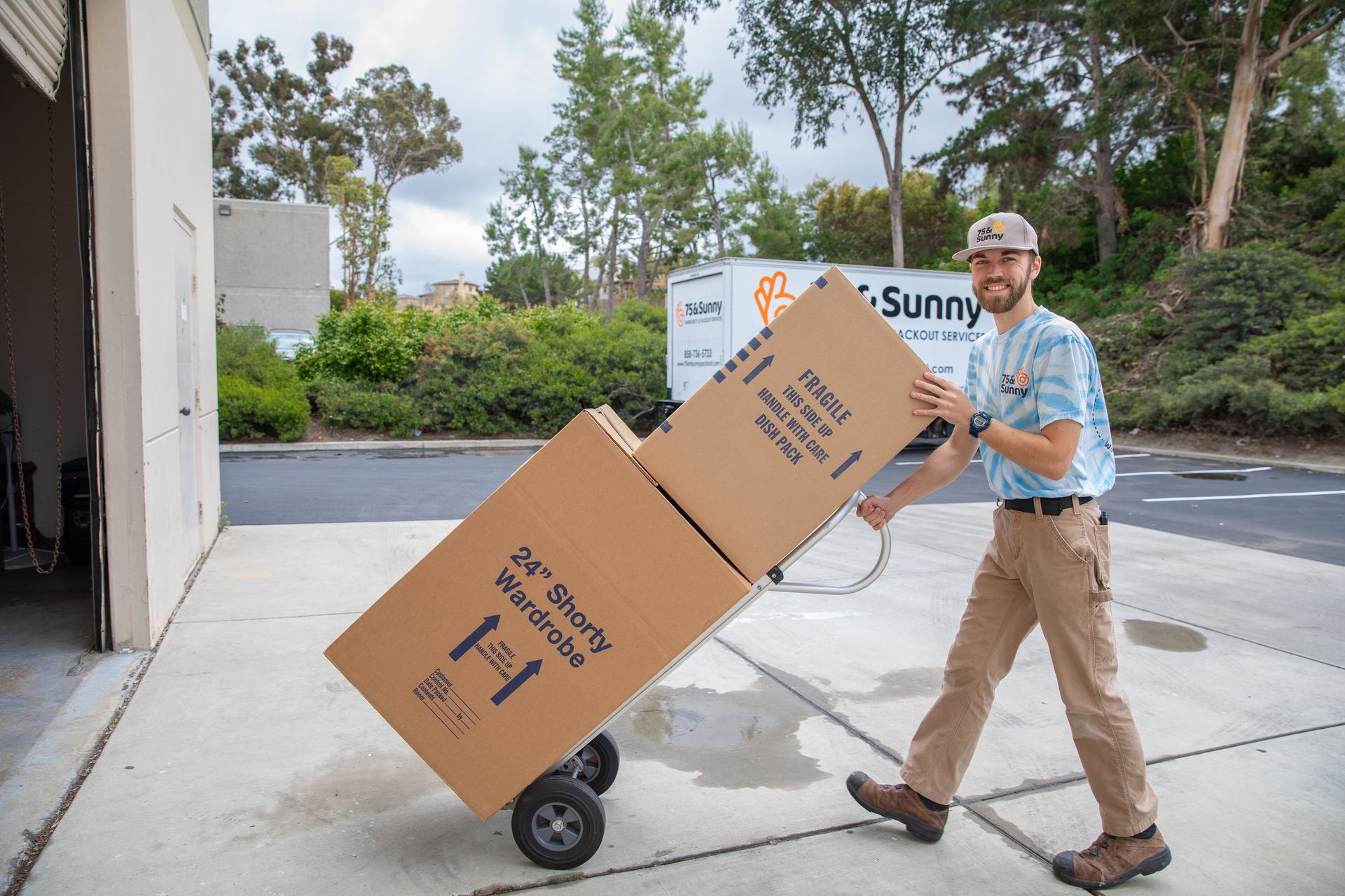 A man is pushing a cart full of boxes that say sunny