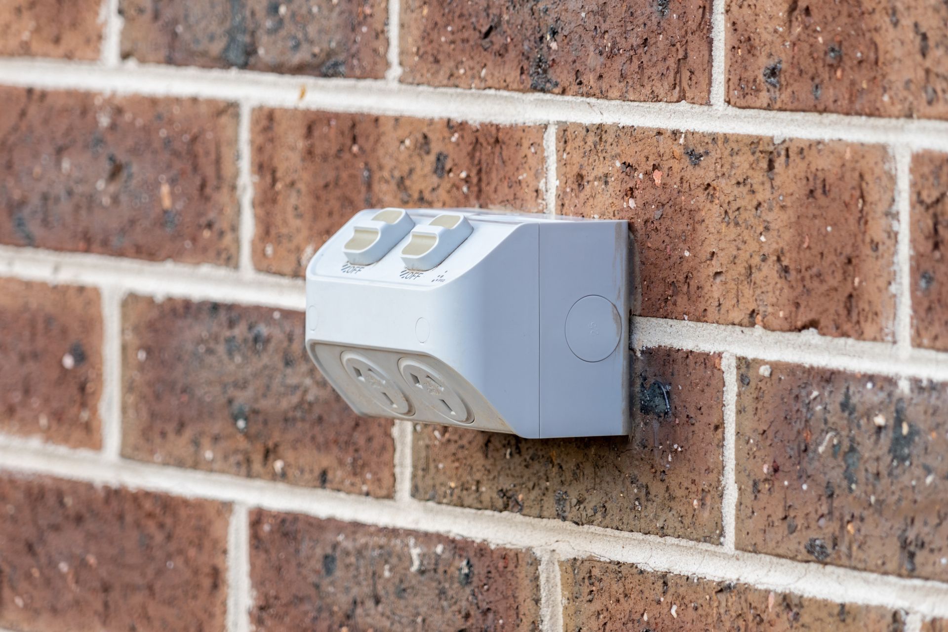 A white electrical outlet is attached to a brick wall. — Greg Keft Electrical in Port Macquarie, NSW