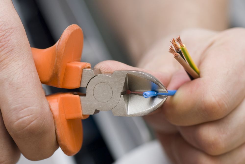 A person is cutting a wire with a pair of pliers. — Greg Keft Electrical in Port Macquarie, NSW