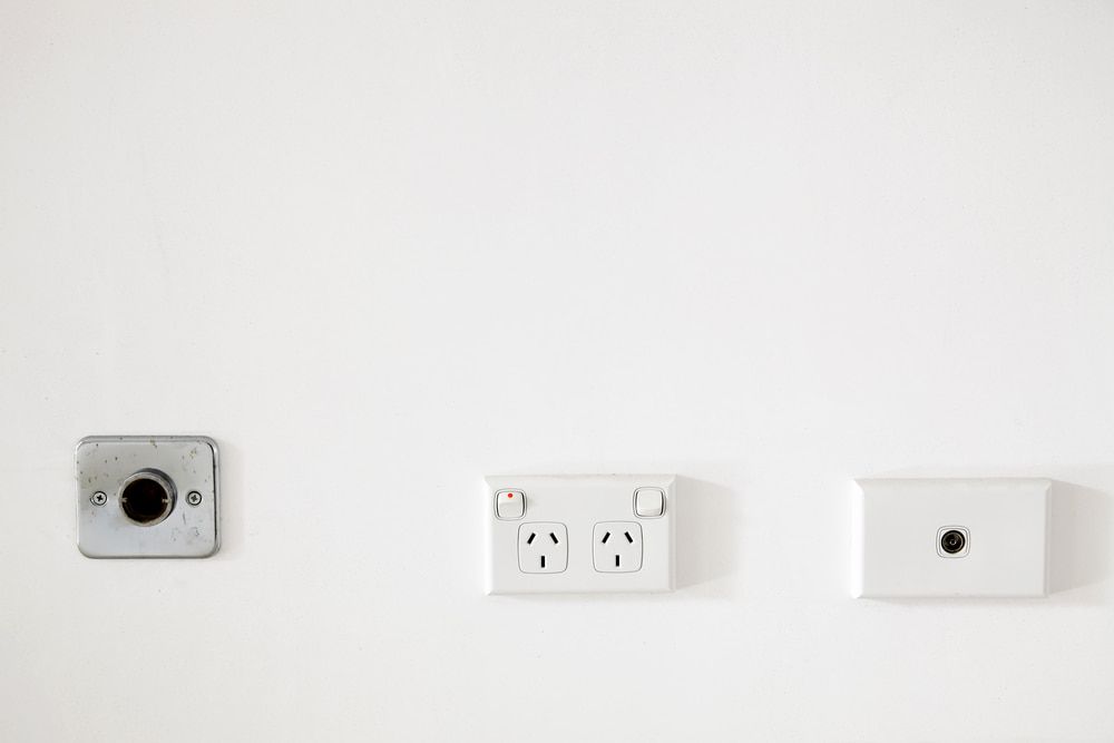 A White Wall With Three Electrical Outlets And A Light Switch — Greg Keft Electrical in Port Macquarie, NSW
