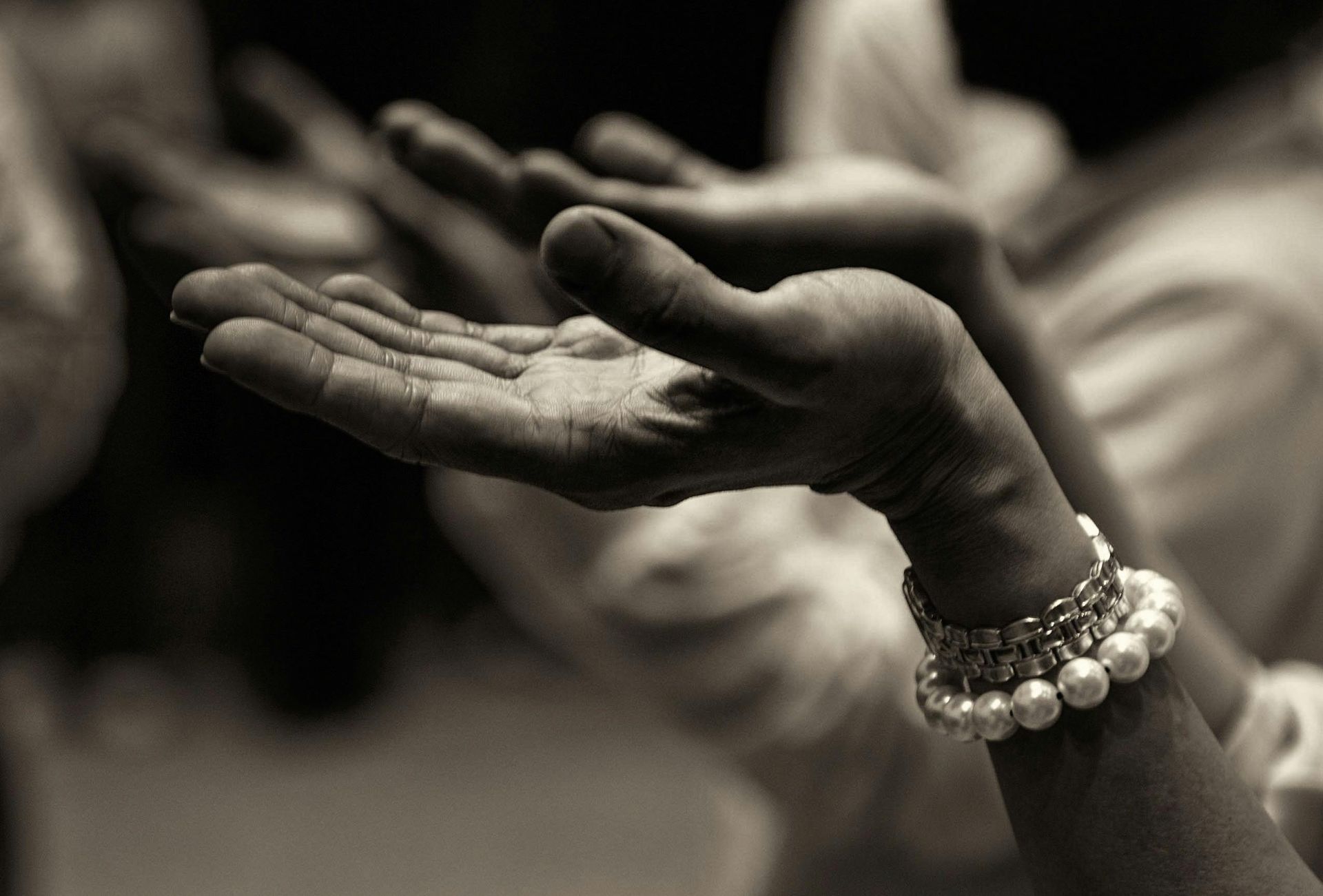 Hands with open palms, wearing a bracelet, reaching upwards, likely in prayer or offering.