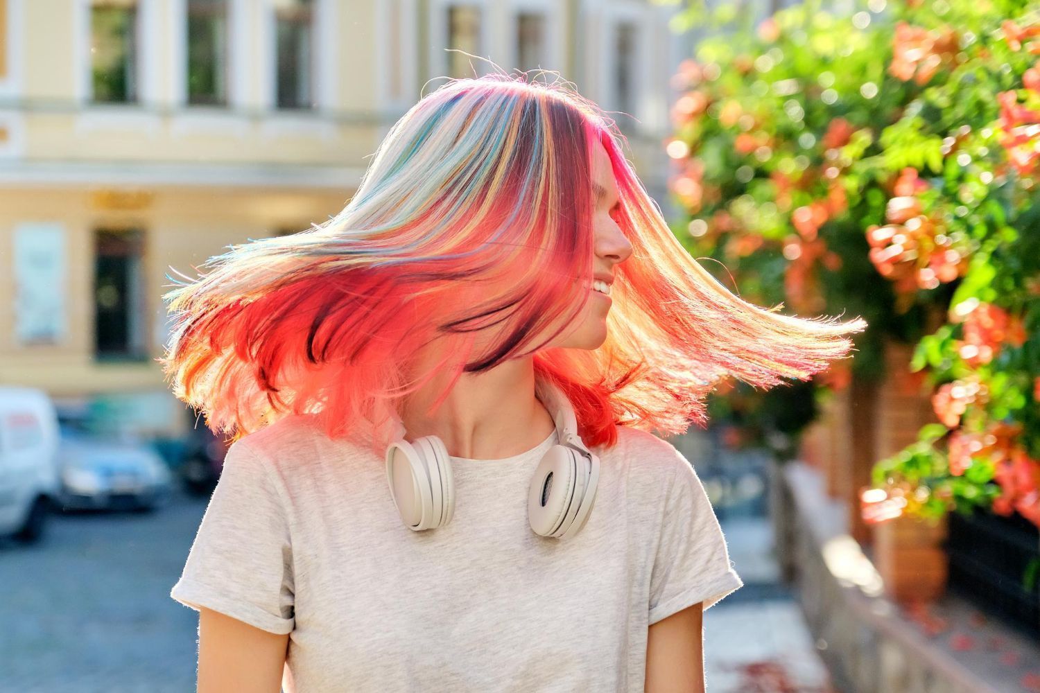 A woman with pink hair and headphones is walking down the street.