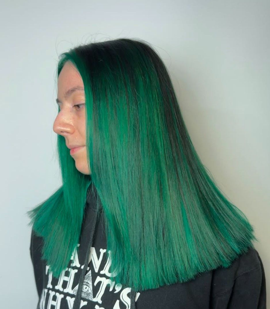 A woman with long green hair is wearing a black hoodie.