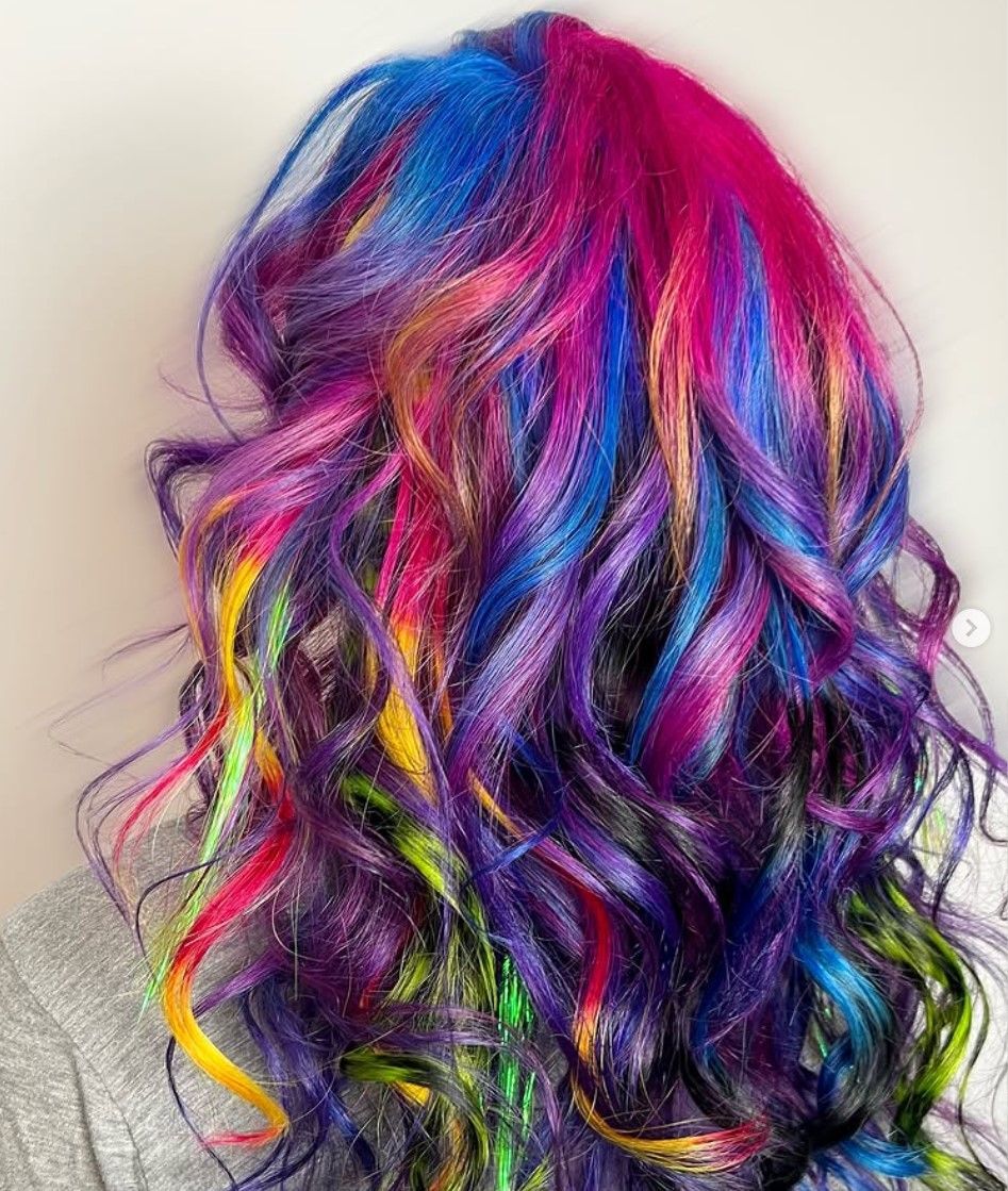 A woman with rainbow hair is standing in front of a white wall.