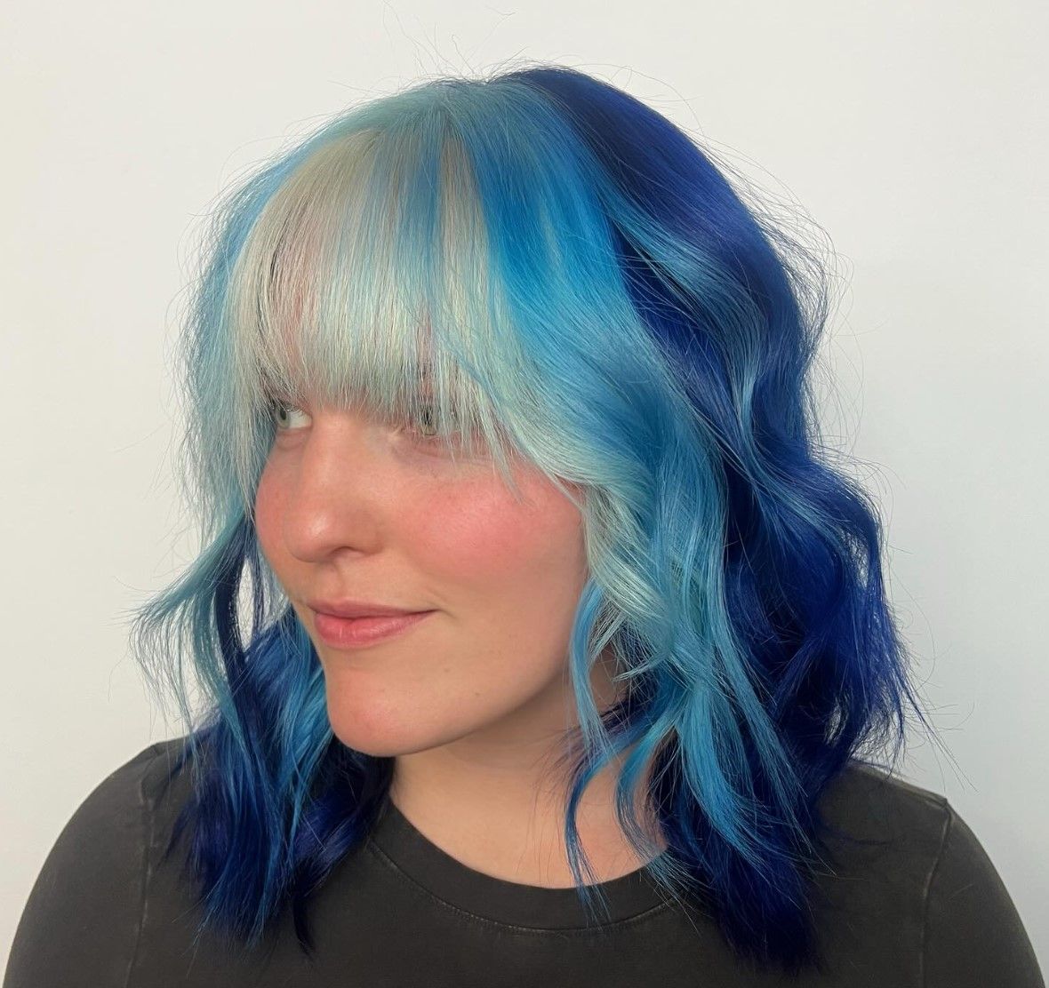 A woman with blue and white hair and bangs is wearing a black shirt.
