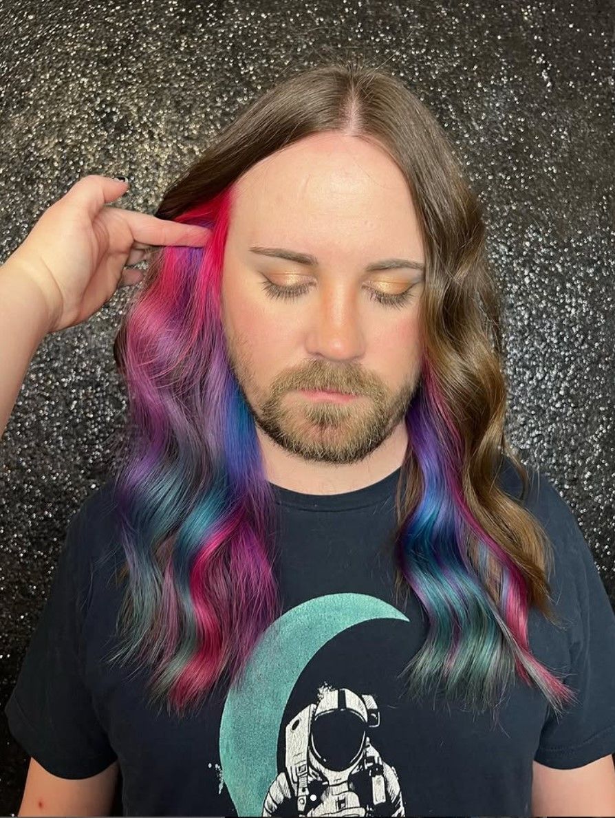 A man with a beard and long hair is getting his hair dyed.
