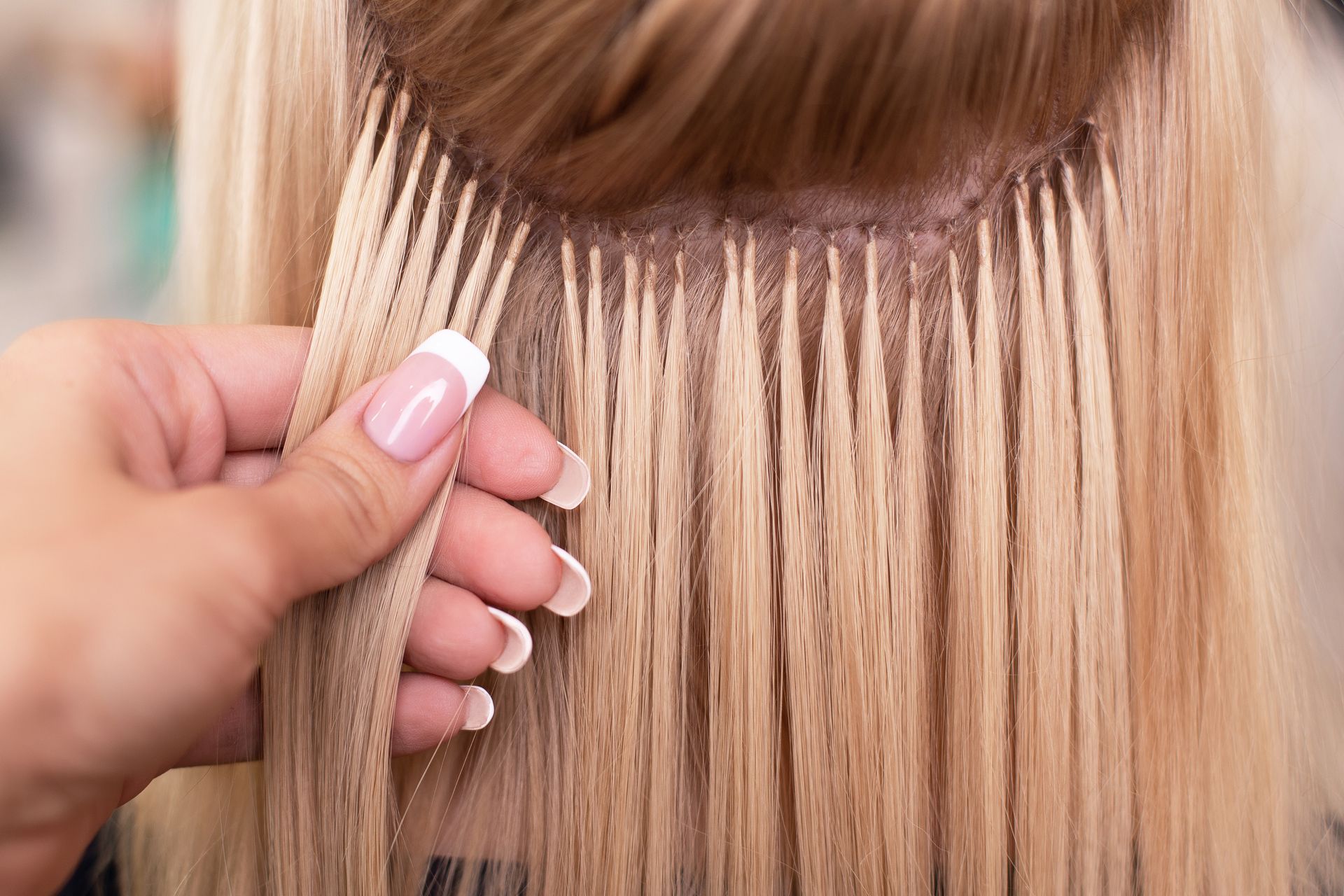 Blonde hair extensions attached to natural hair with a hand holding a strand.