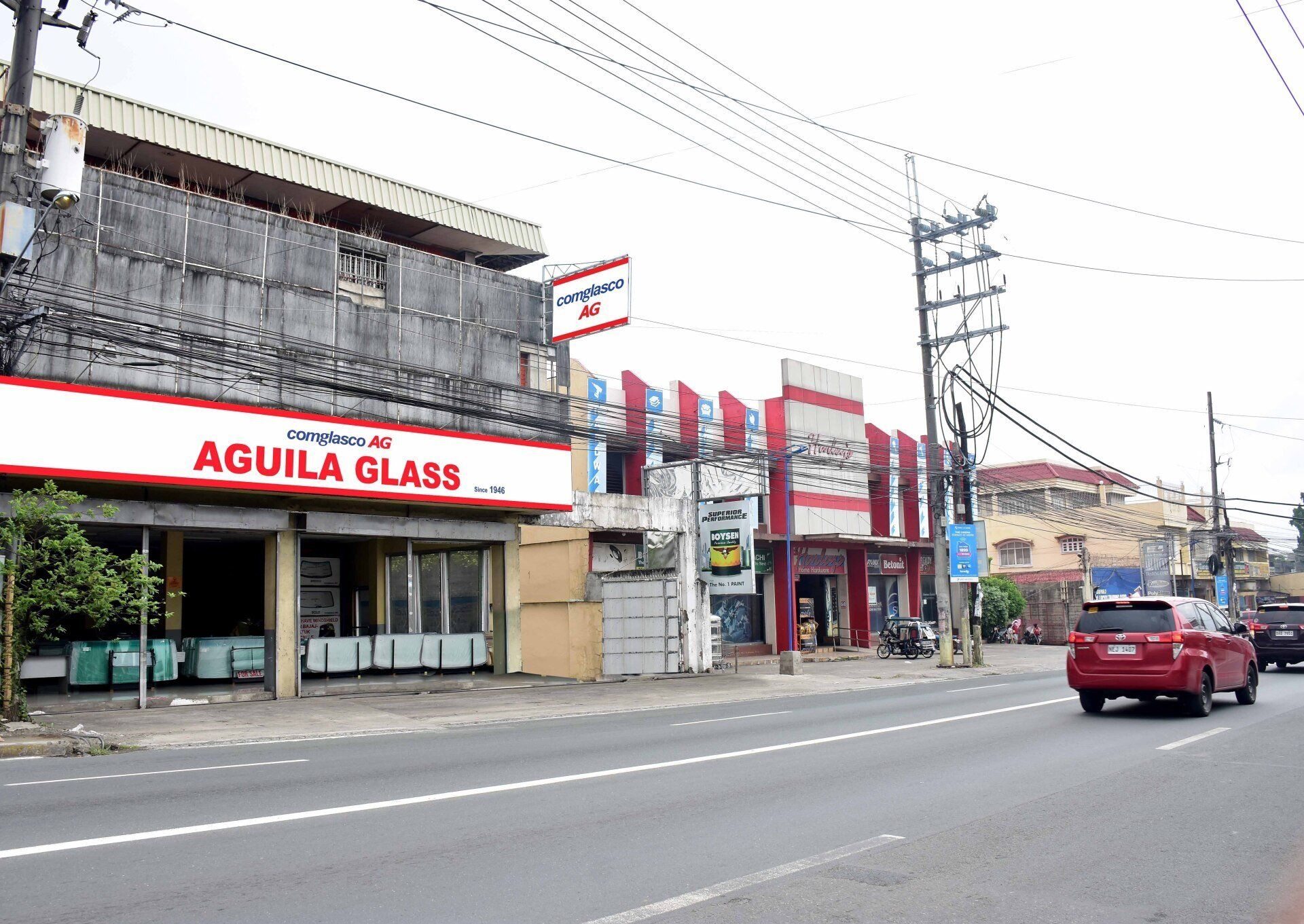 A red car is driving past a building that says aguila glass