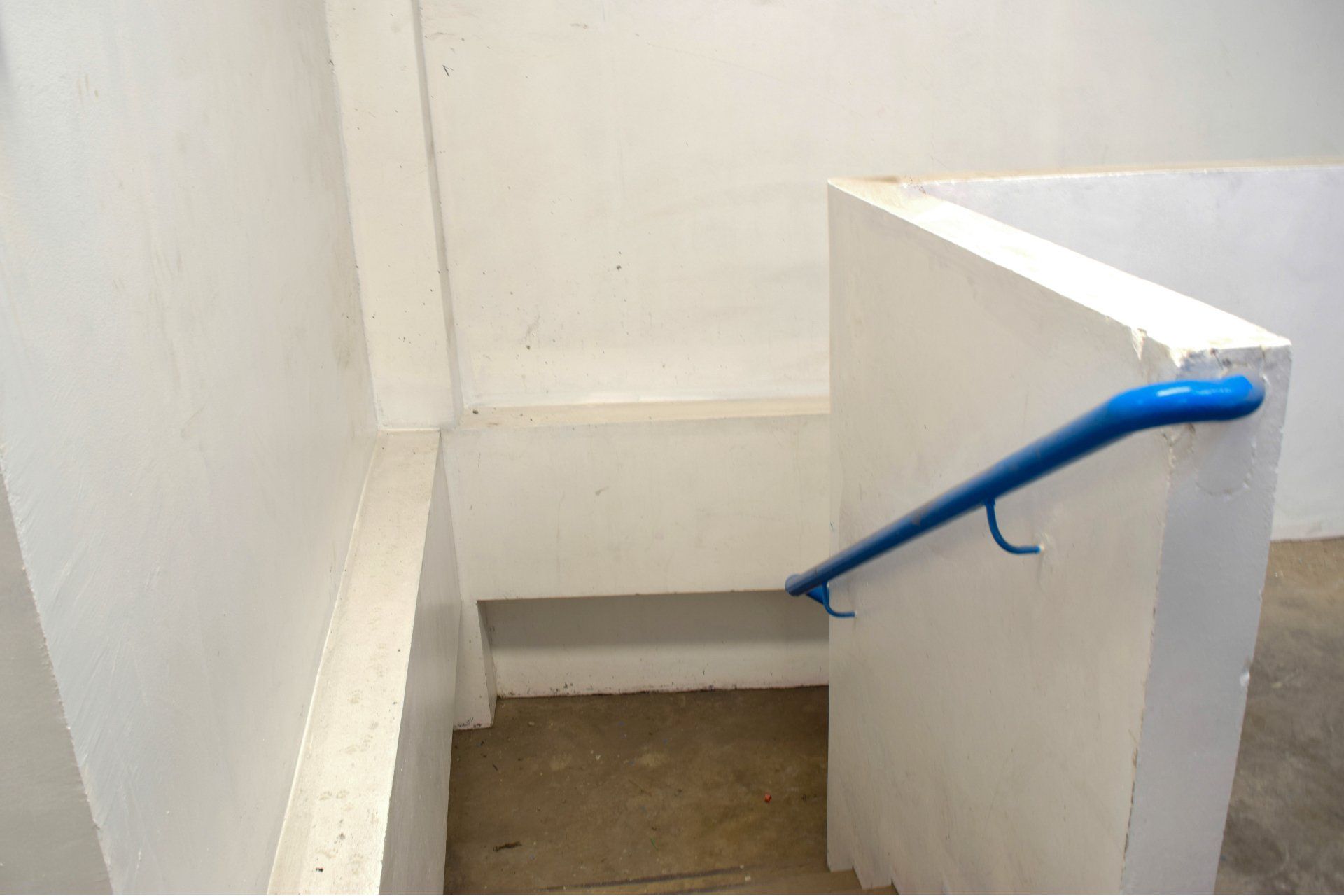 A blue handrail is attached to a white wall.