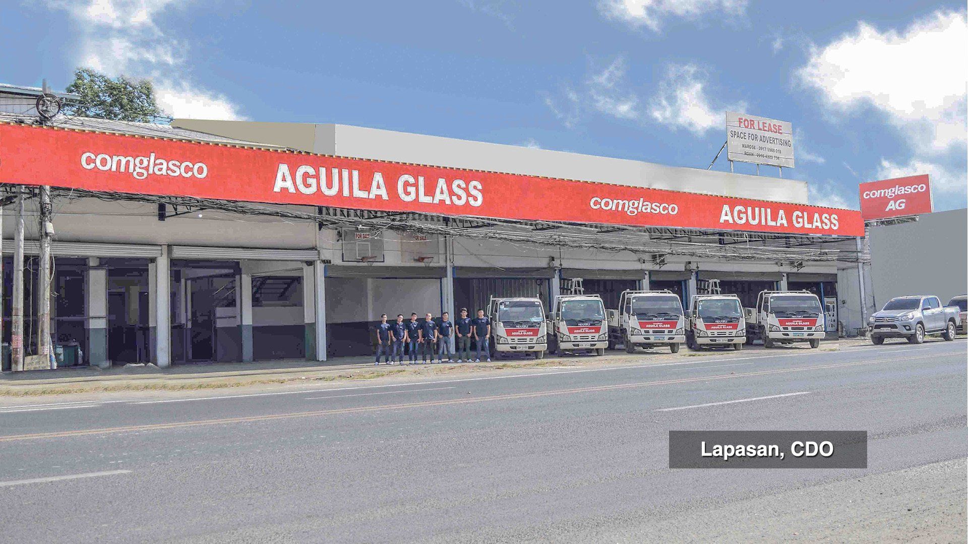 A row of cars are parked in front of a building that says aguila glass