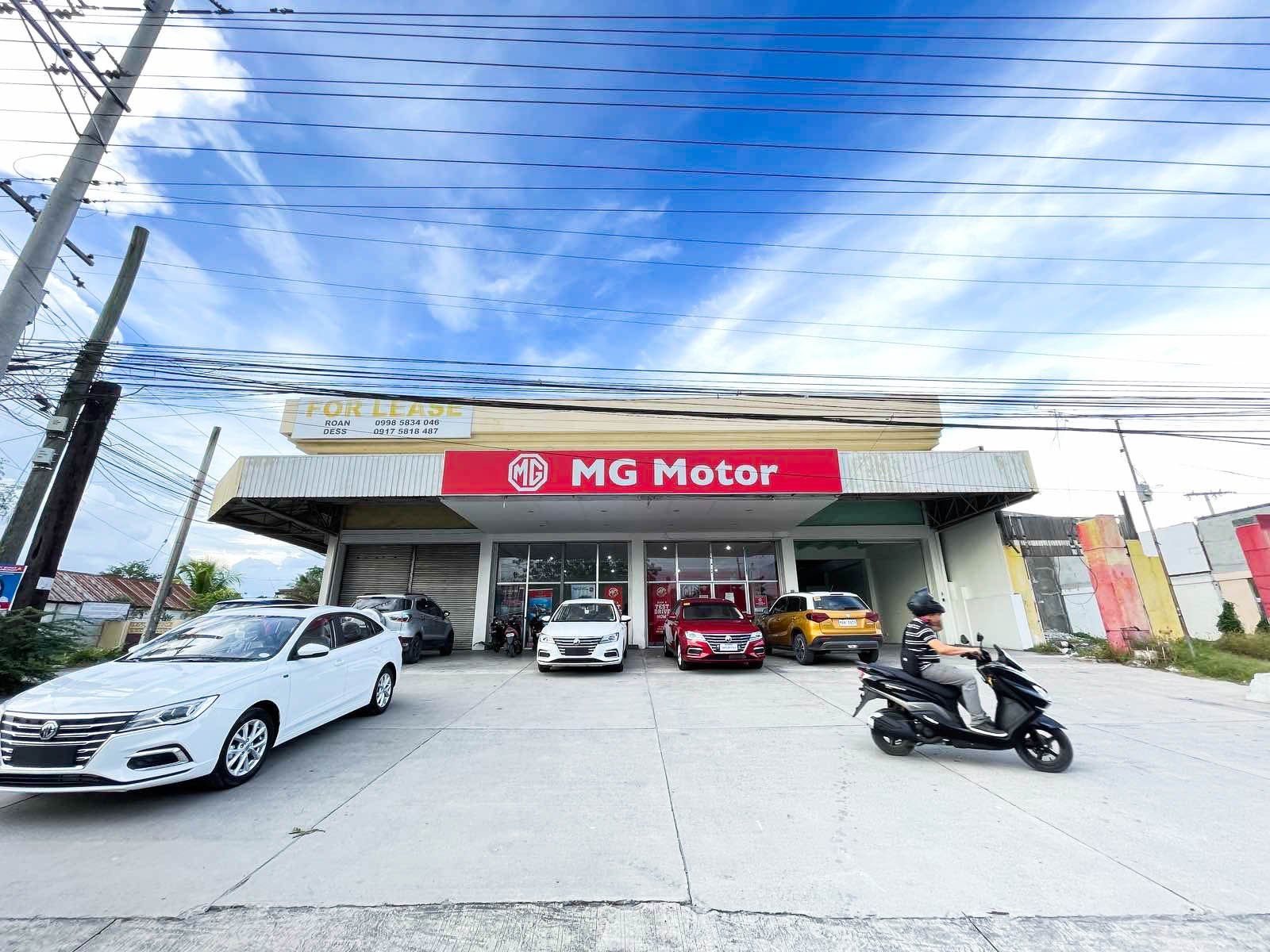 A group of cars are parked in front of a mg motor car dealership.