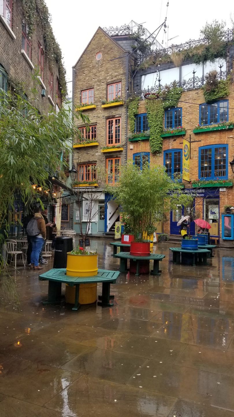 Courtyard with colorful buildings, tables, and trees; raining.