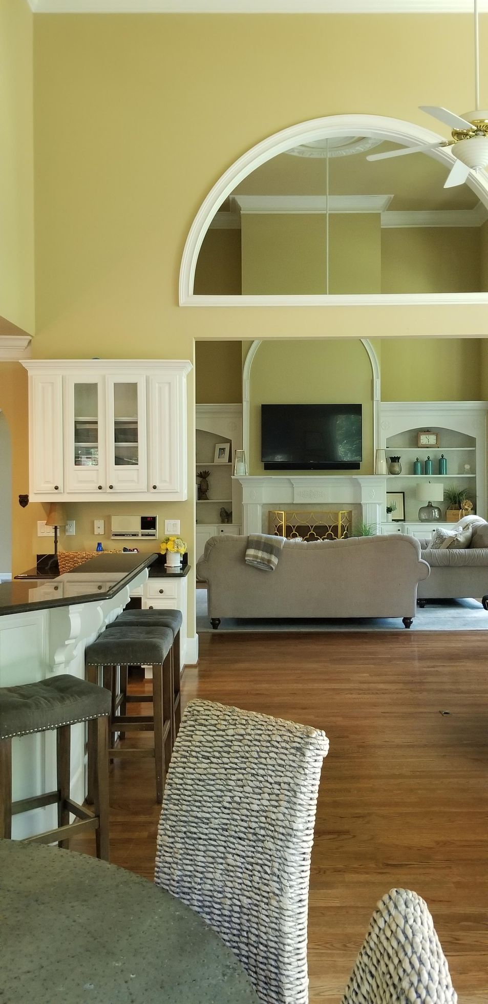 Interior view of a kitchen and living room with hardwood floors, a bar, a sofa, and a TV.