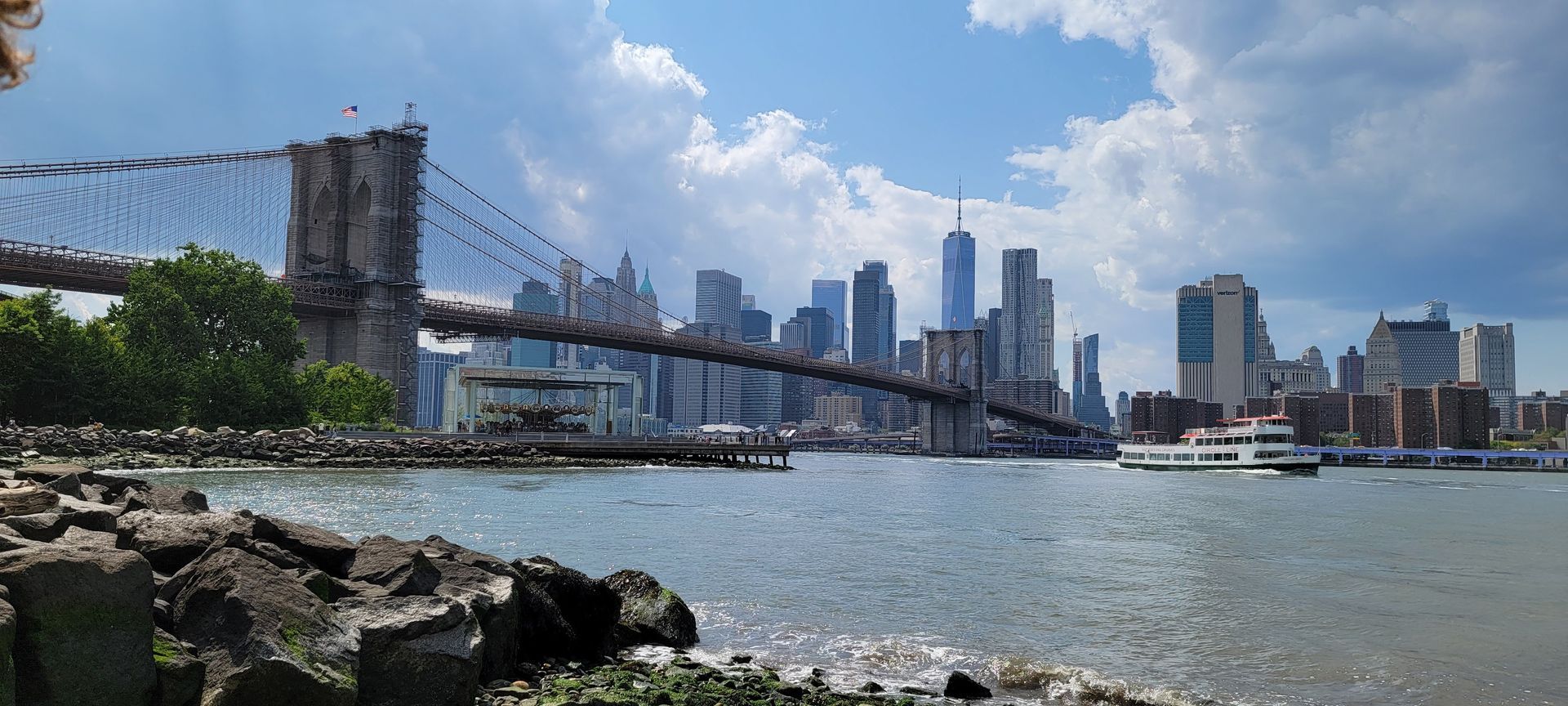 Brooklyn Bridge over water, cityscape of skyscrapers, sunny day.