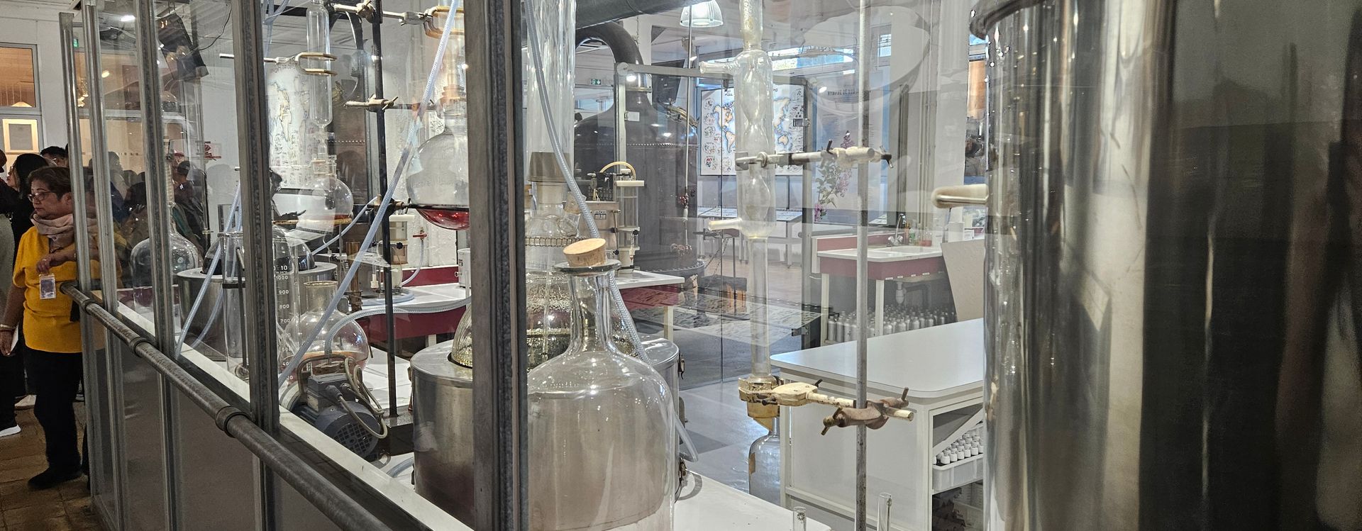 Glass apparatus in a laboratory setting with people visible in the periphery.