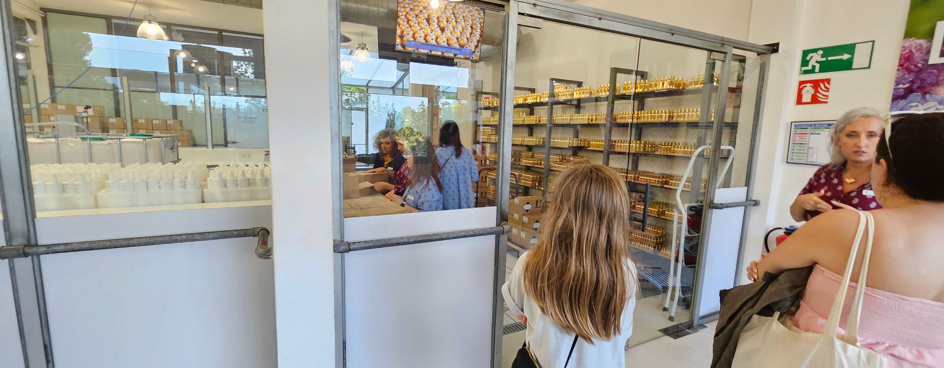 People inside a store with glass windows. Shelves of merchandise and a woman assisting customers.