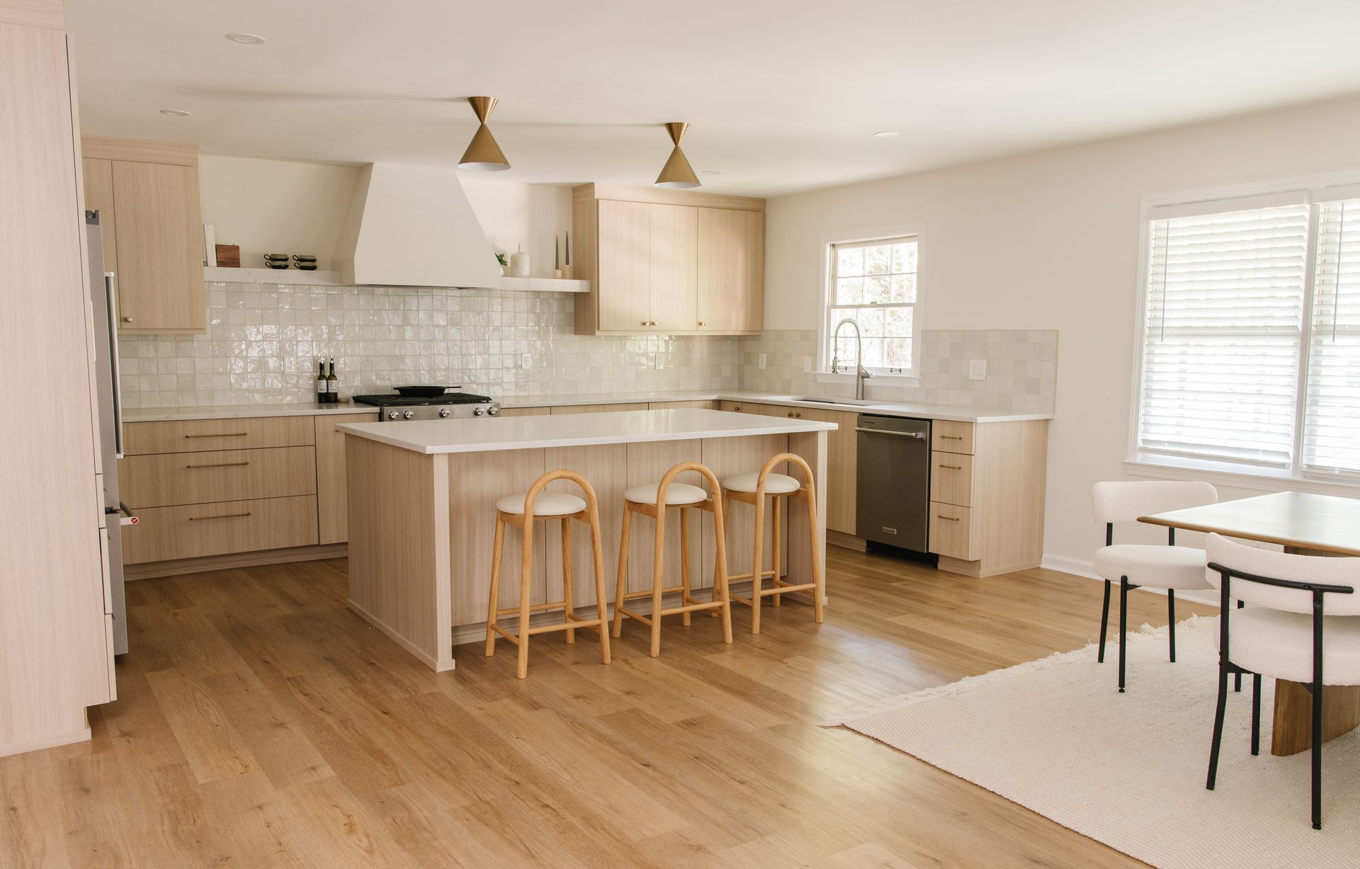 Bright, modern kitchen with light wood cabinets, white countertops, and bar stools around a central island.