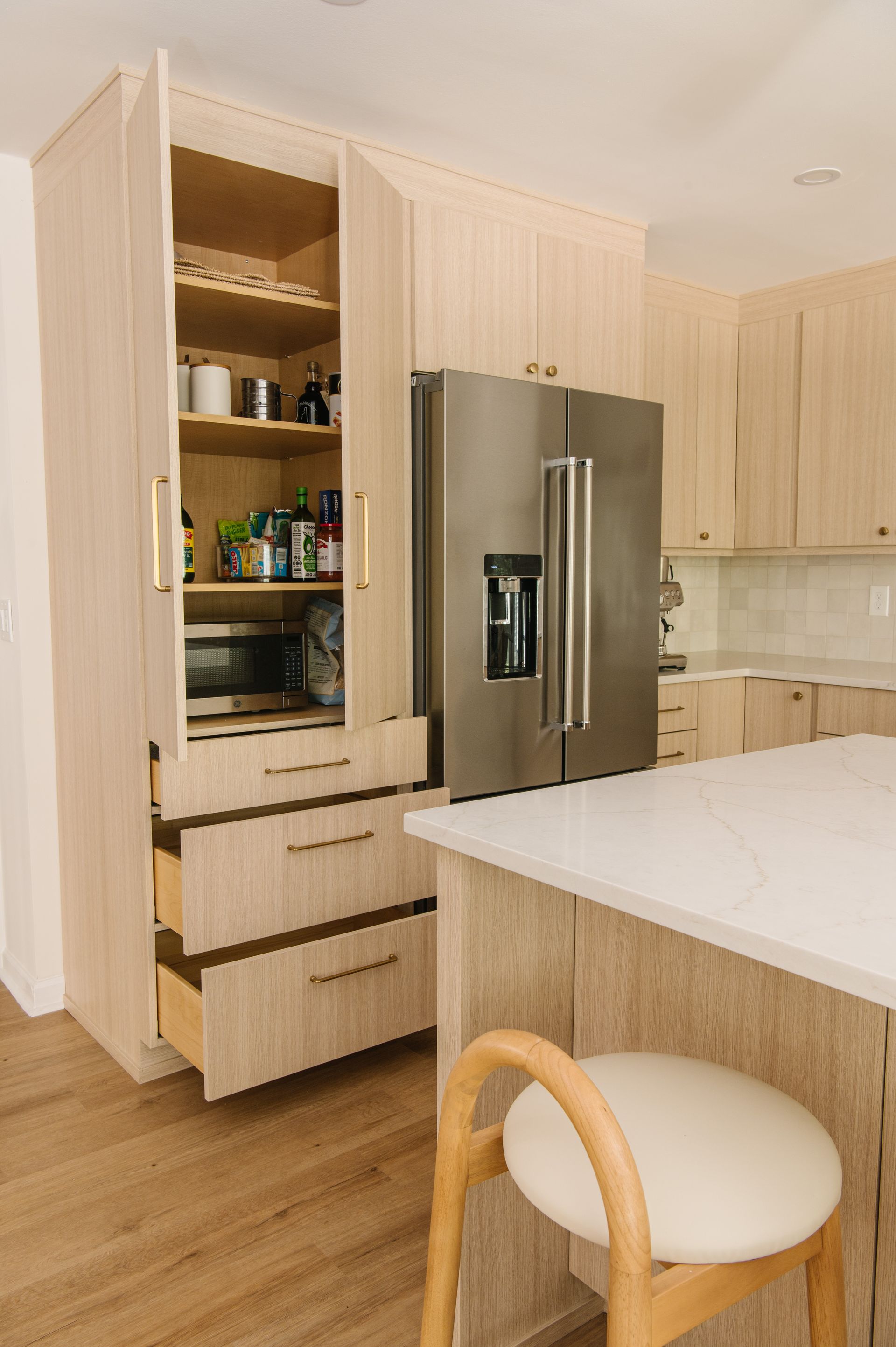 Beige kitchen with open pantry, built-in microwave, and stainless steel refrigerator.  Light wood cabinets and flooring.