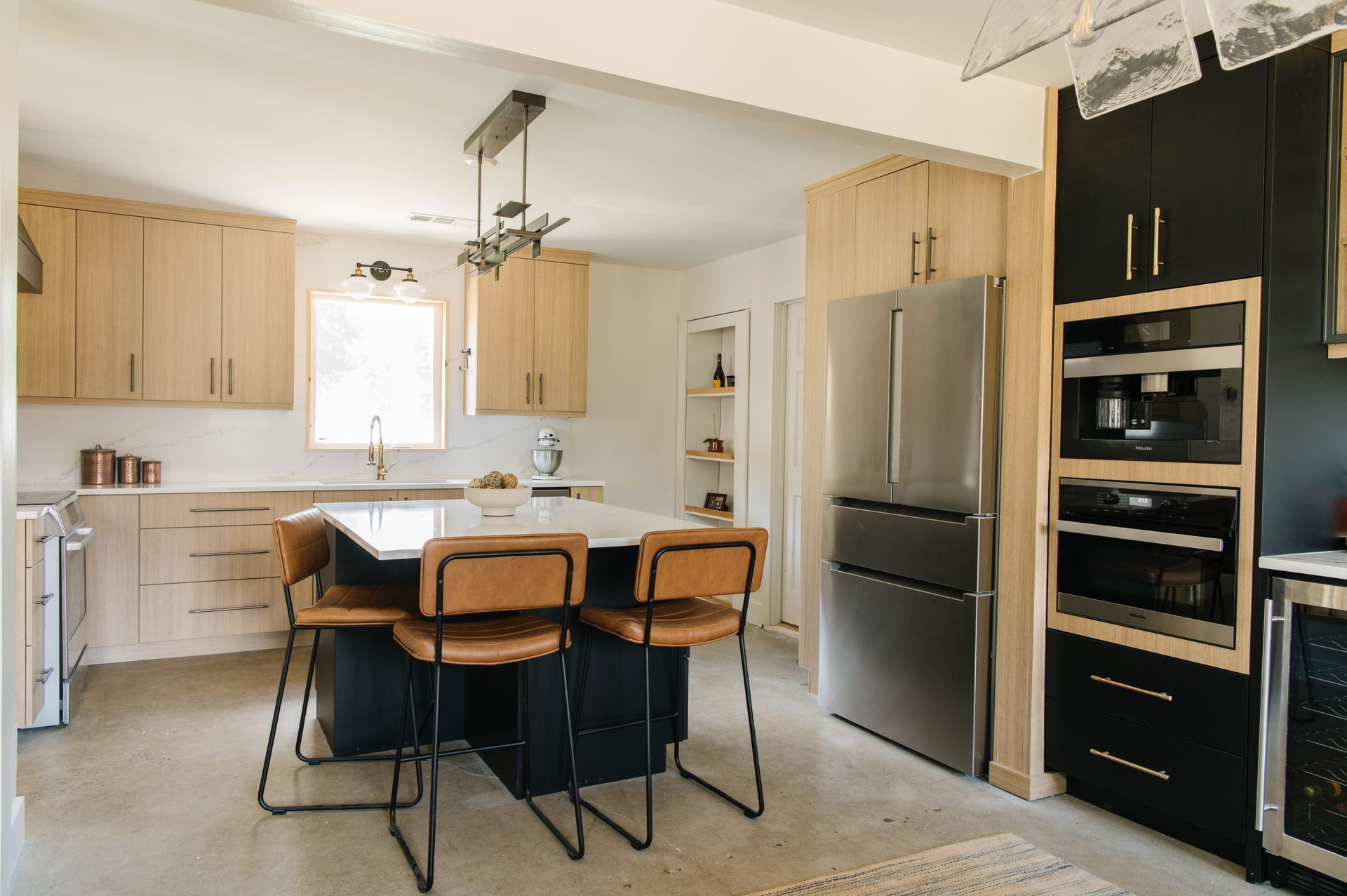 Modern kitchen with light wood cabinets, dark island with brown bar stools, stainless steel appliances.