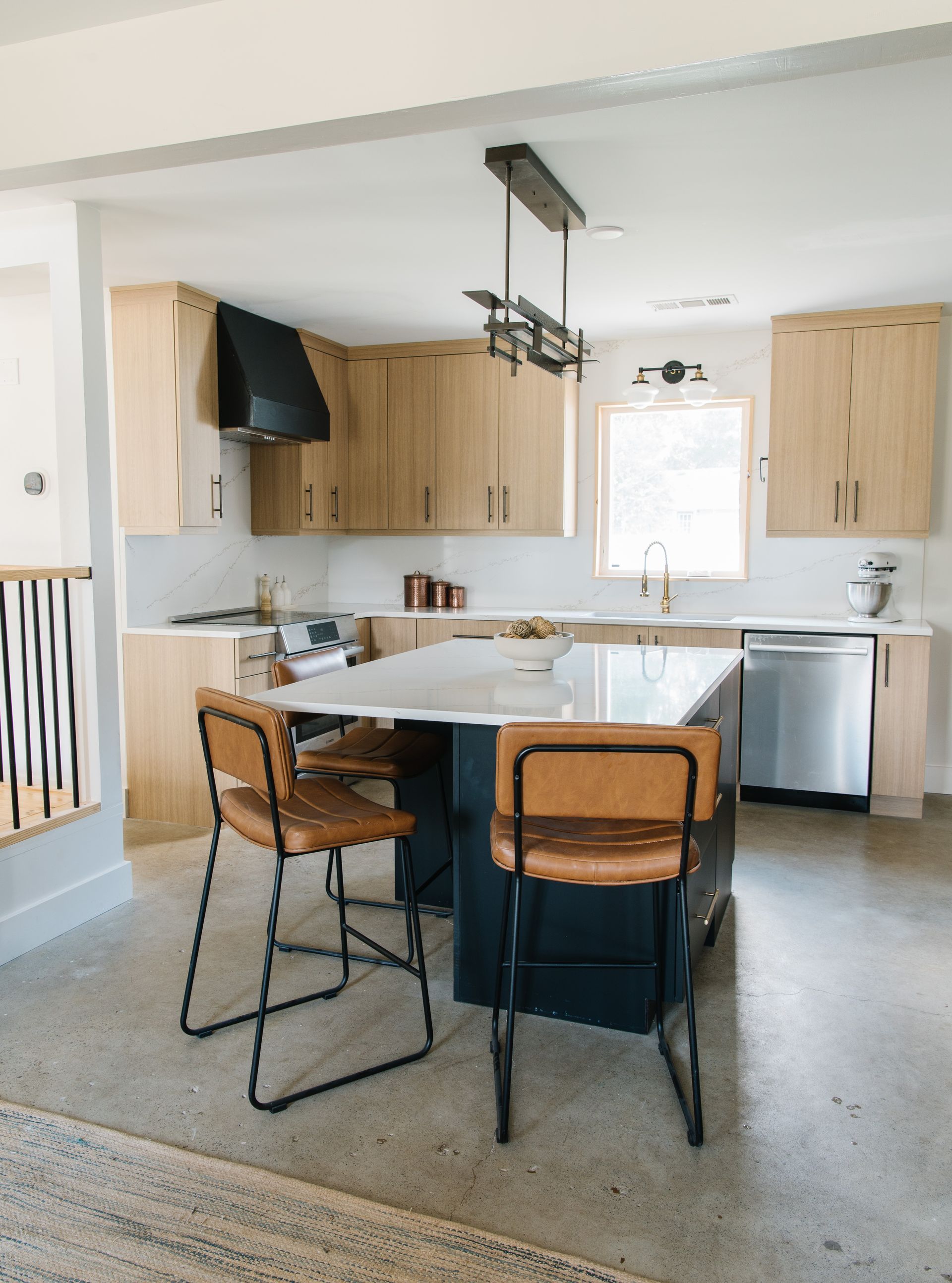Modern kitchen with light wood cabinets, dark island, and leather bar stools.