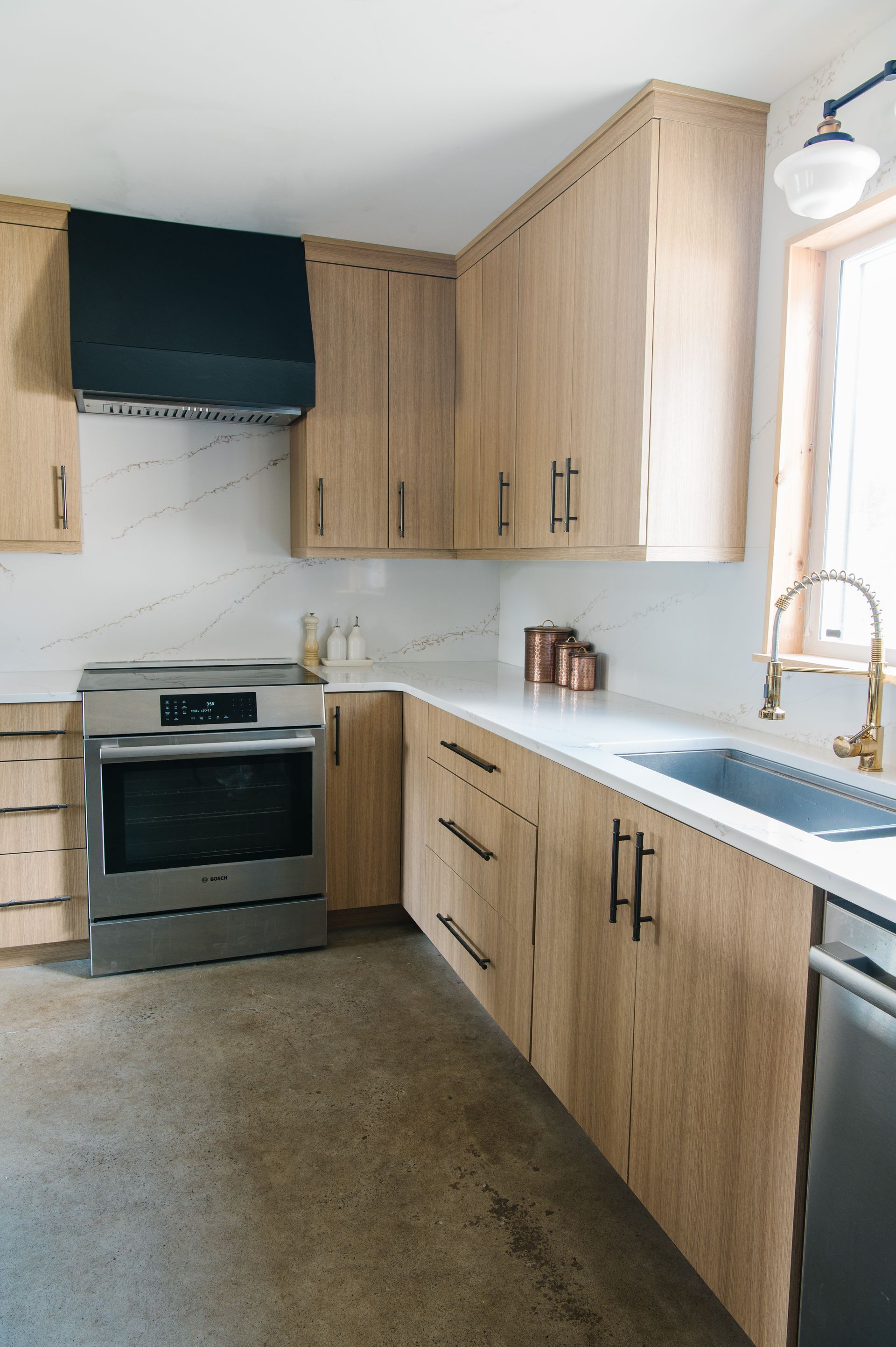 A modern kitchen with light wood cabinets, stainless steel appliances, and a black range hood.