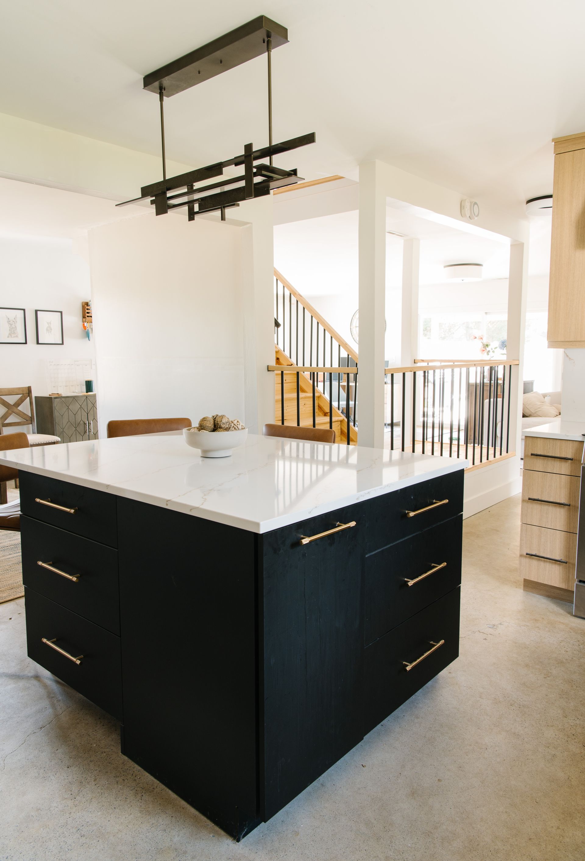 Black kitchen island with white countertop, gold hardware, and modern light fixture.