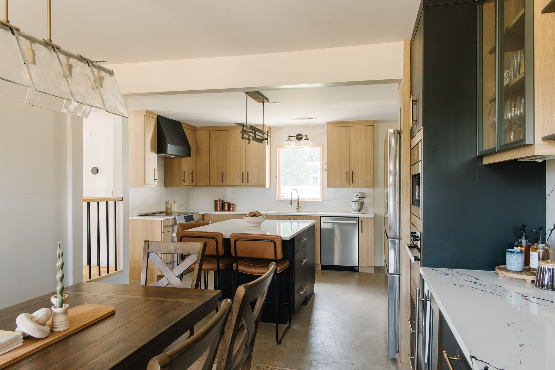 Modern kitchen with island, light wood cabinets, stainless steel appliances, and dark accents.