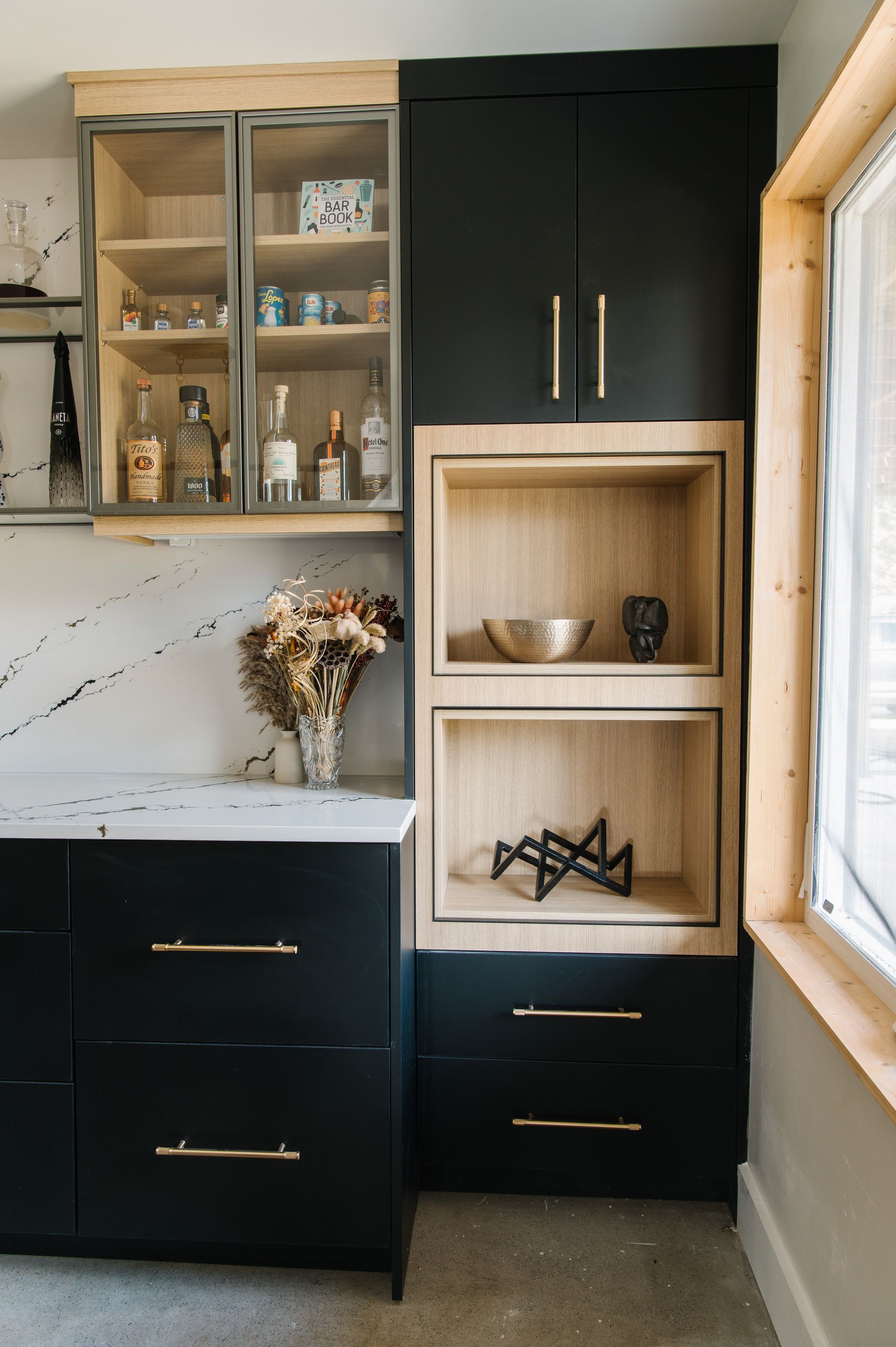 Black kitchen cabinets with gold hardware and light wood shelves.