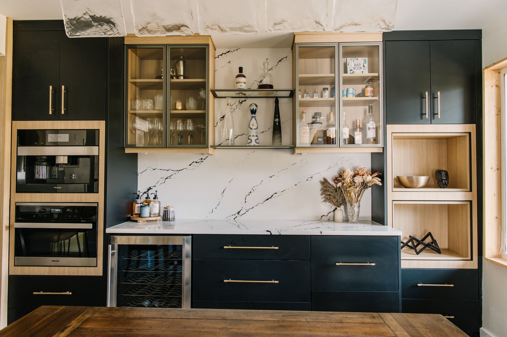 Modern kitchen with dark cabinets, marble backsplash, glass display cabinets, and built-in appliances.