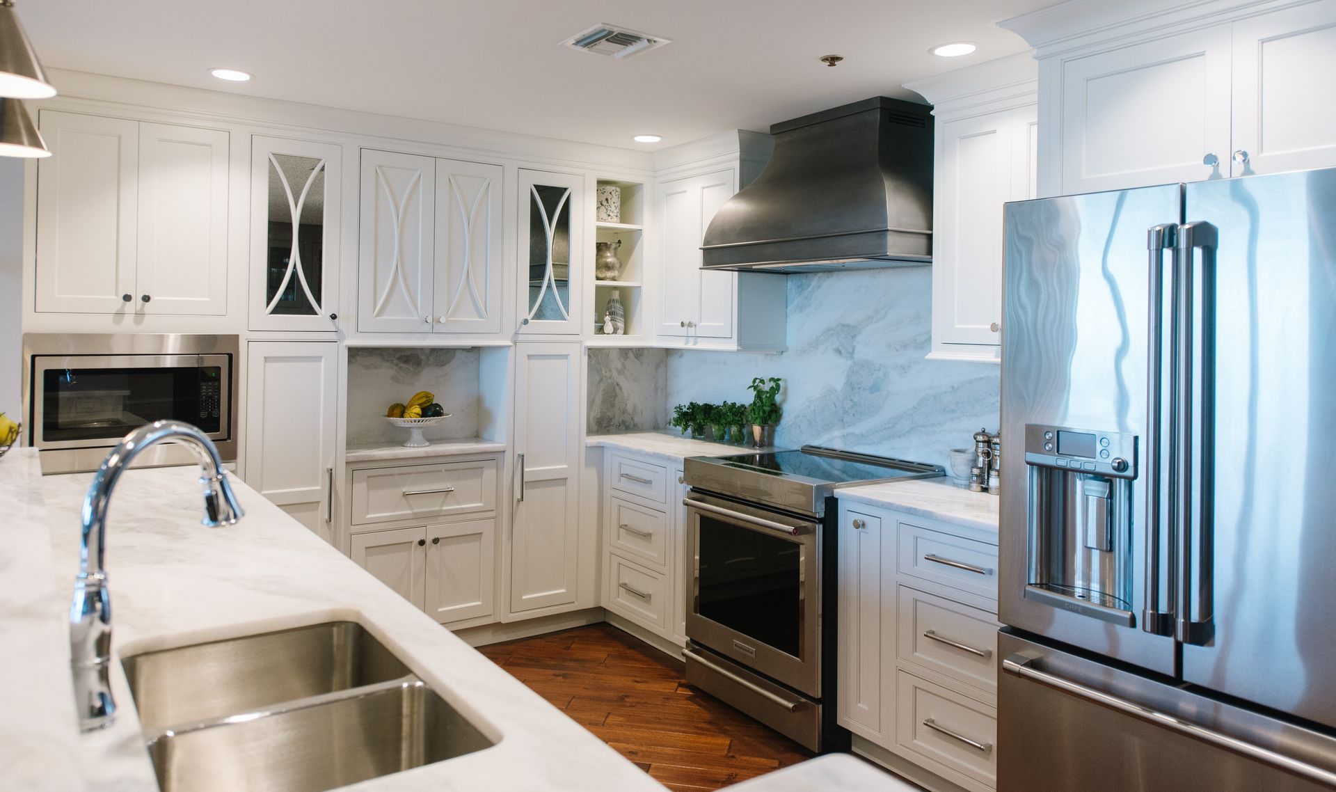 White kitchen with stainless steel appliances, marble countertops, and dark wood floors.