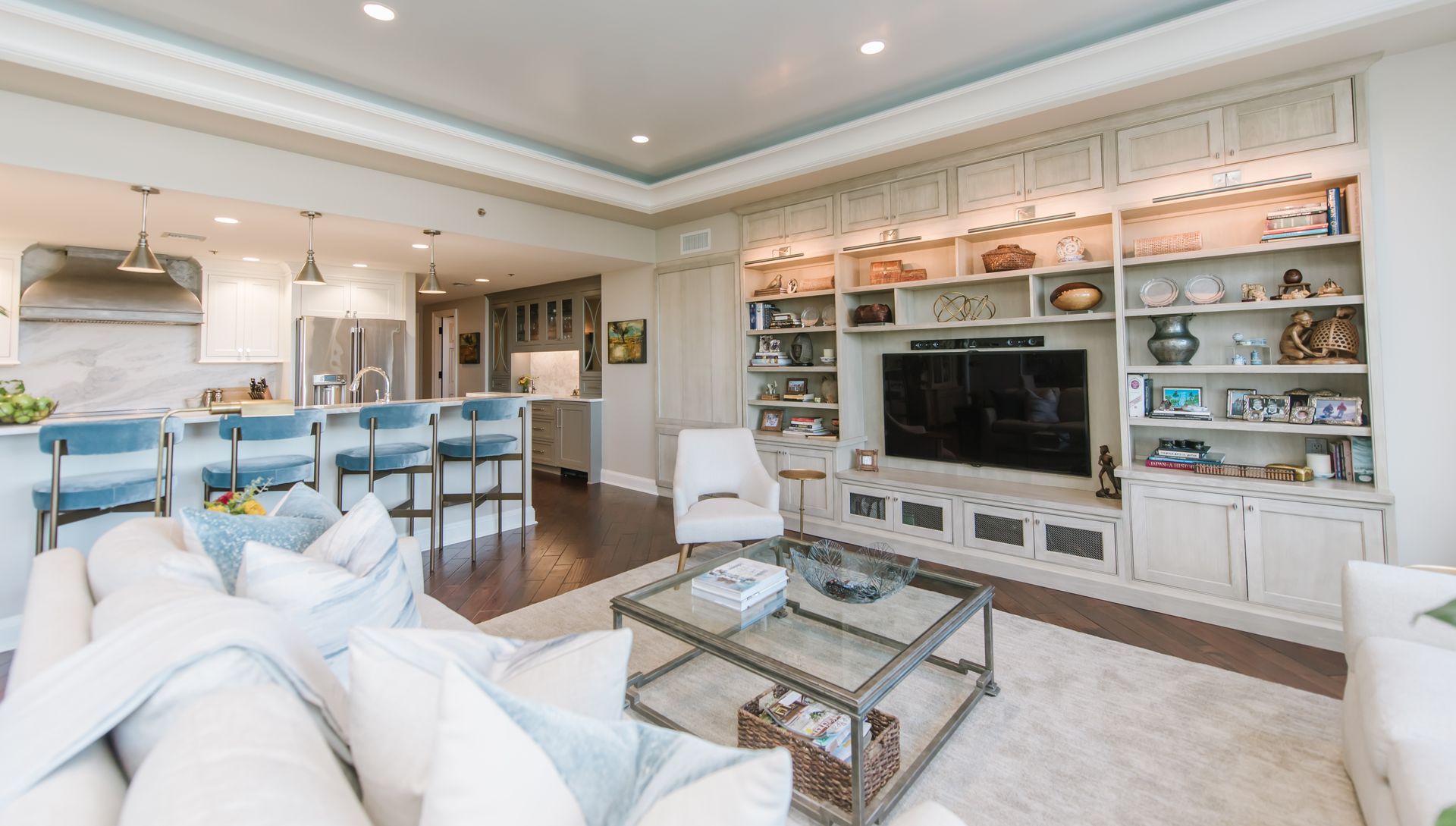 Living room with built-in shelves and entertainment center. White and blue decor. Dark wood floor, and open to the kitchen.