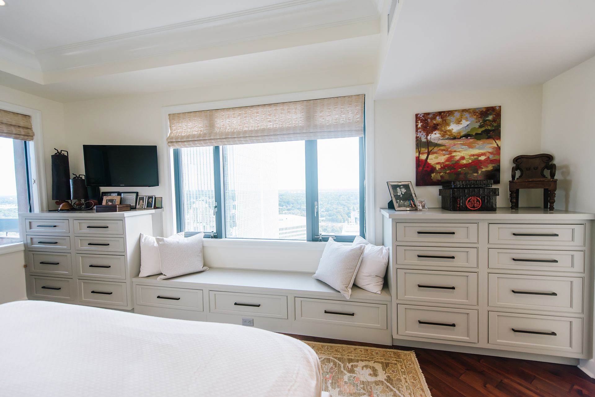 Bedroom with window seat, built-in dressers, TV, and artwork. Natural light and neutral tones.