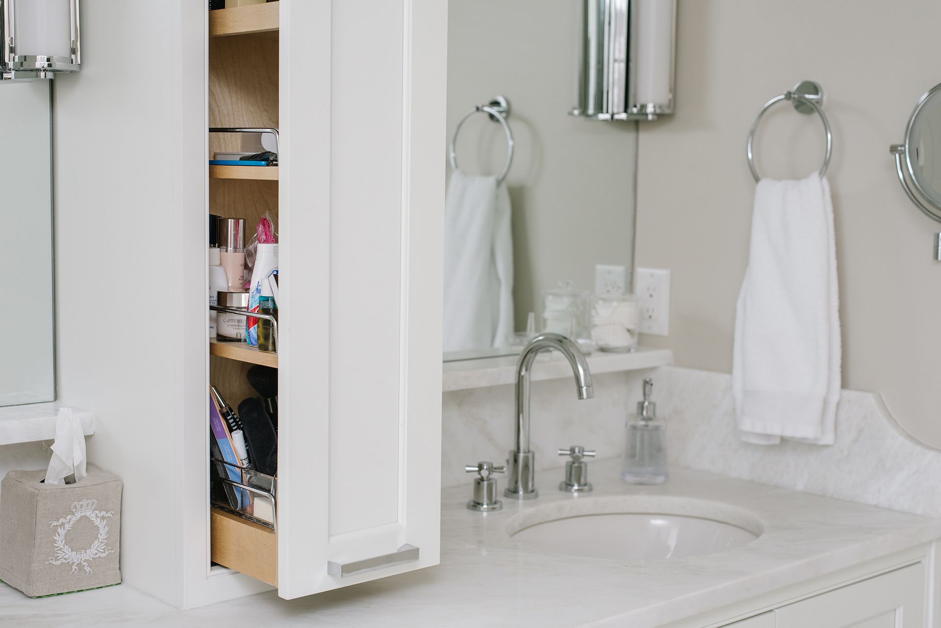 White bathroom vanity with pull-out cabinet open. Sink, faucet, mirror, towels, and tissue box are also visible.