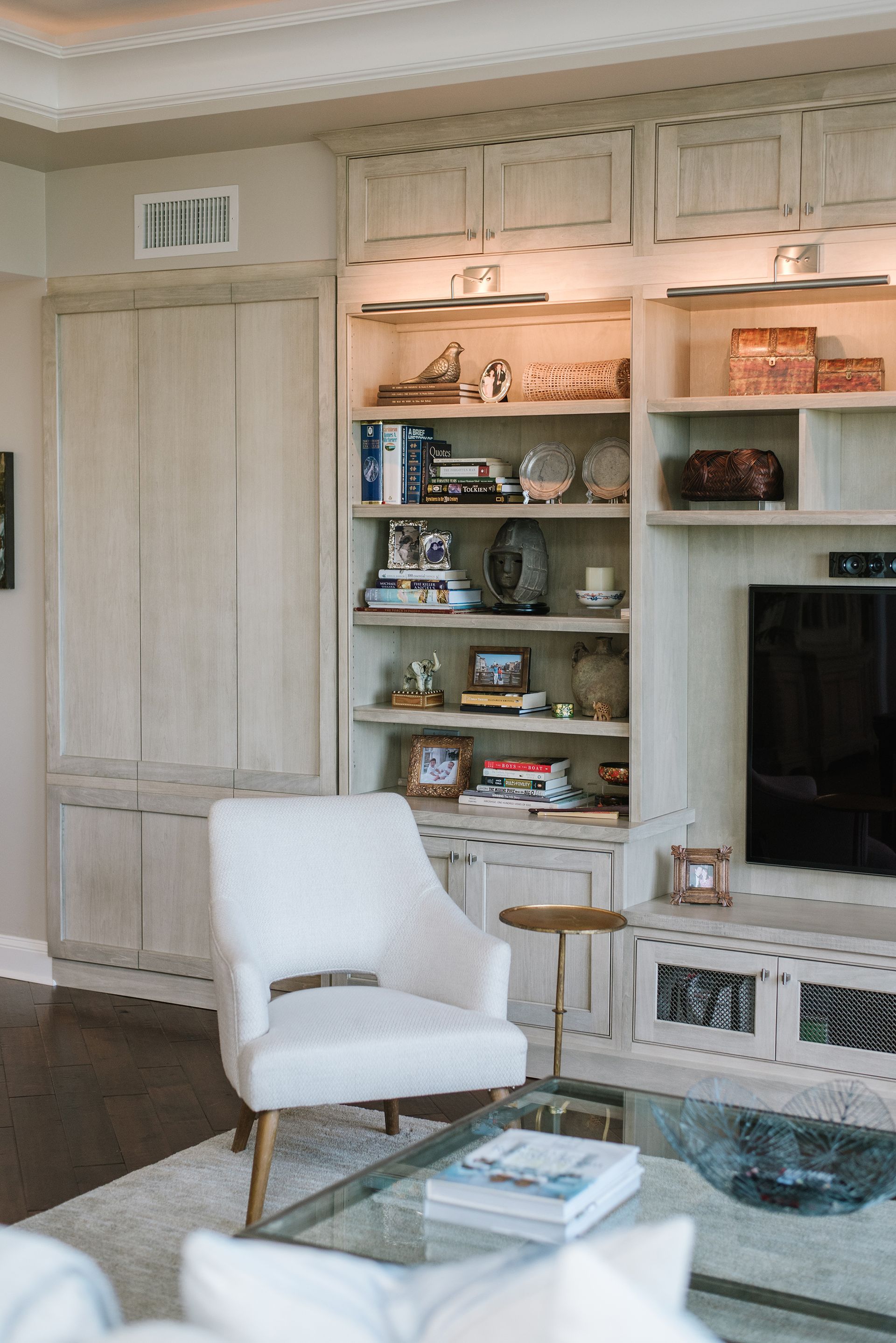 Built-in bookcase with display items, TV, and cream armchair in a living room.