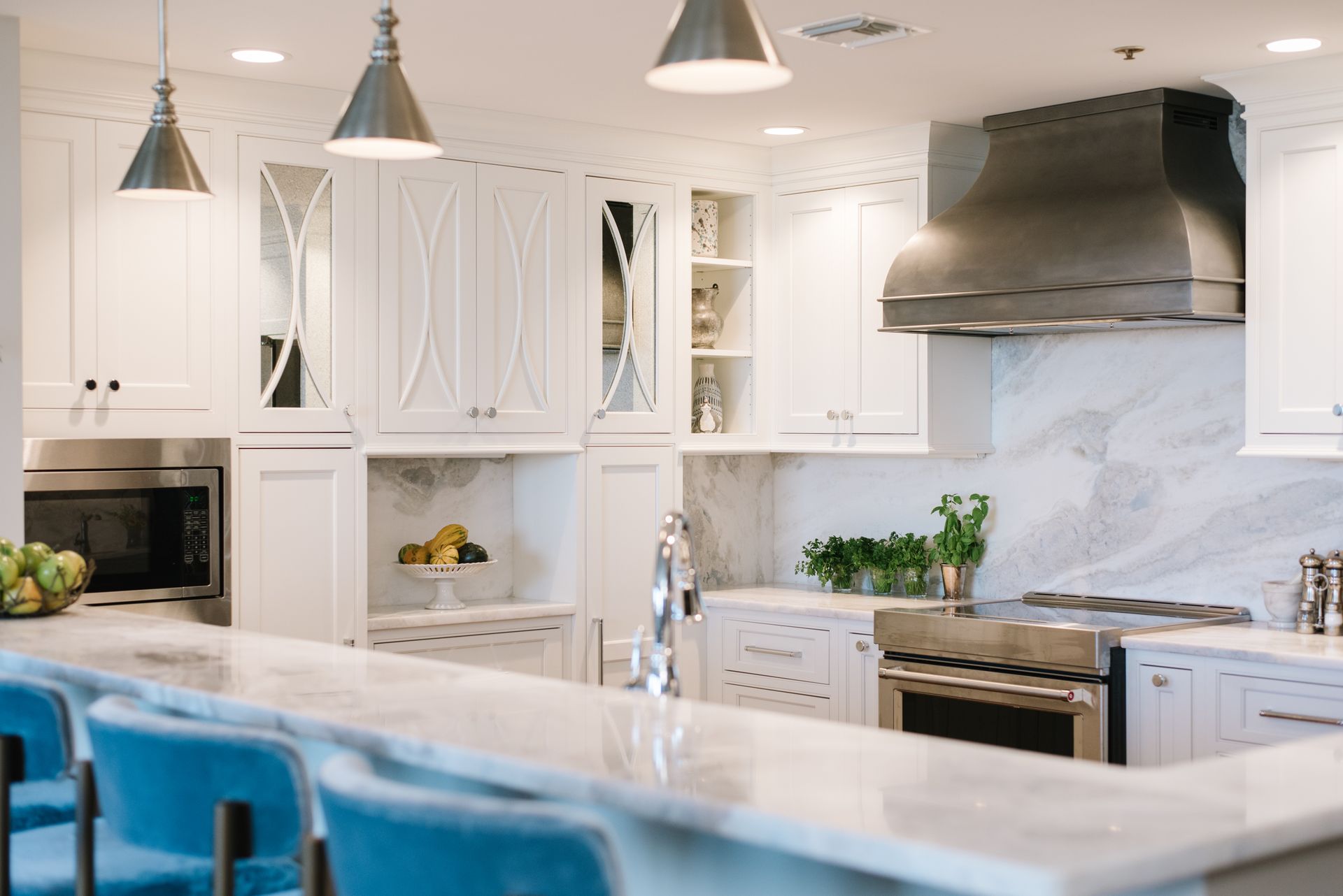 White kitchen with marble countertops, stainless steel appliances, and blue bar stools.