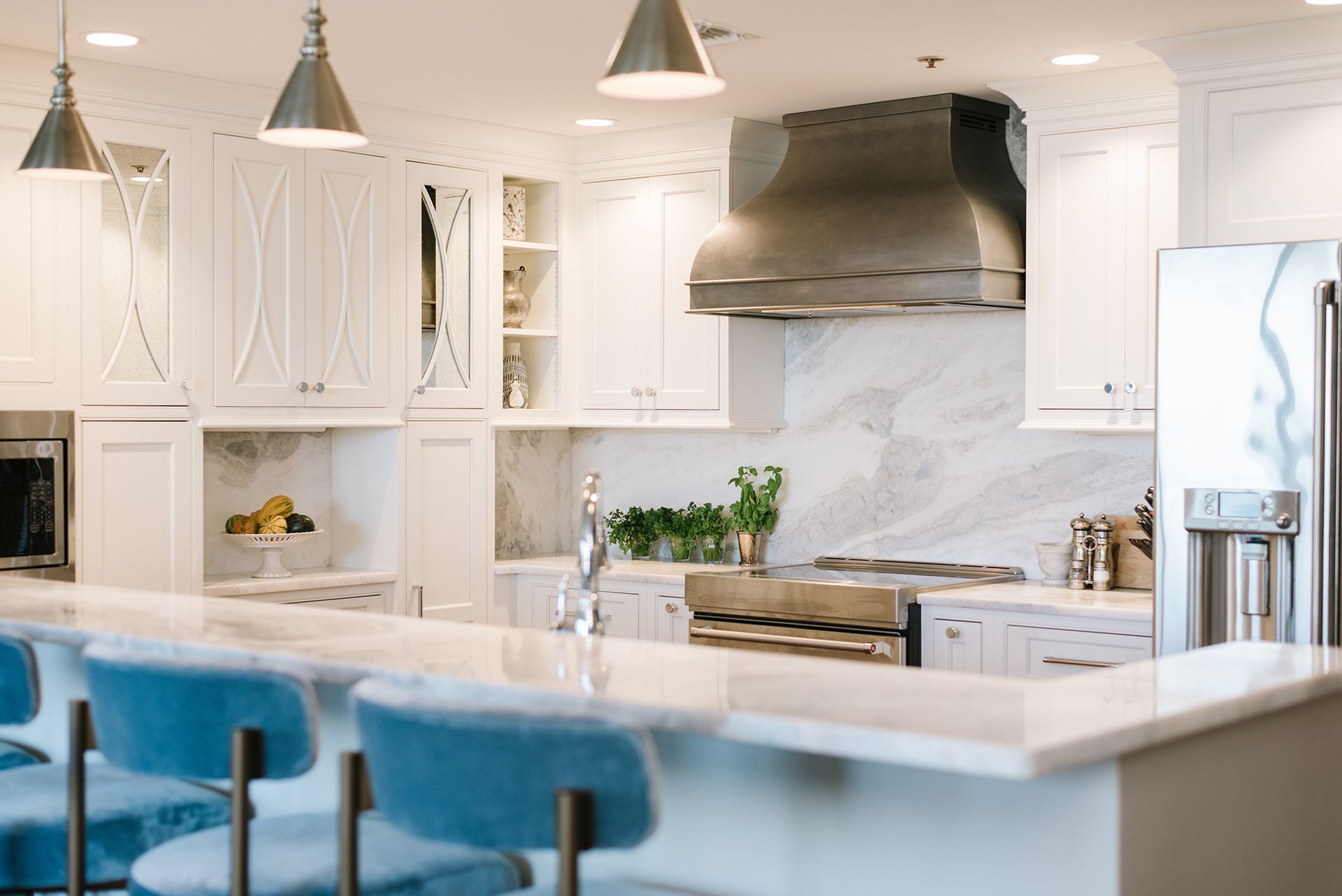 Elegant white kitchen with marble countertops, stainless steel appliances, and blue bar stools.
