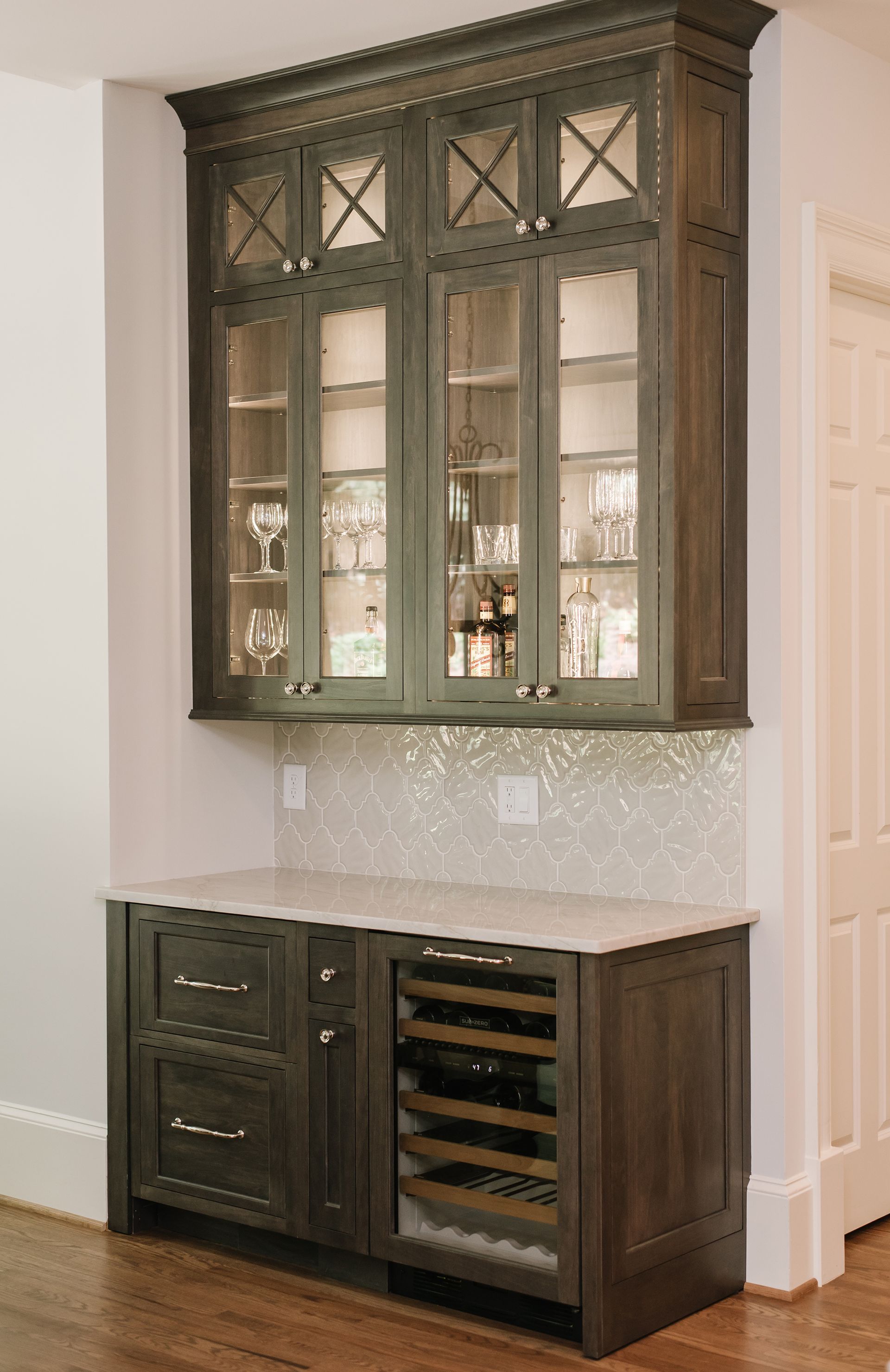 Built-in, dark gray bar cabinet with wine cooler, glass-front upper cabinets, and white countertop.
