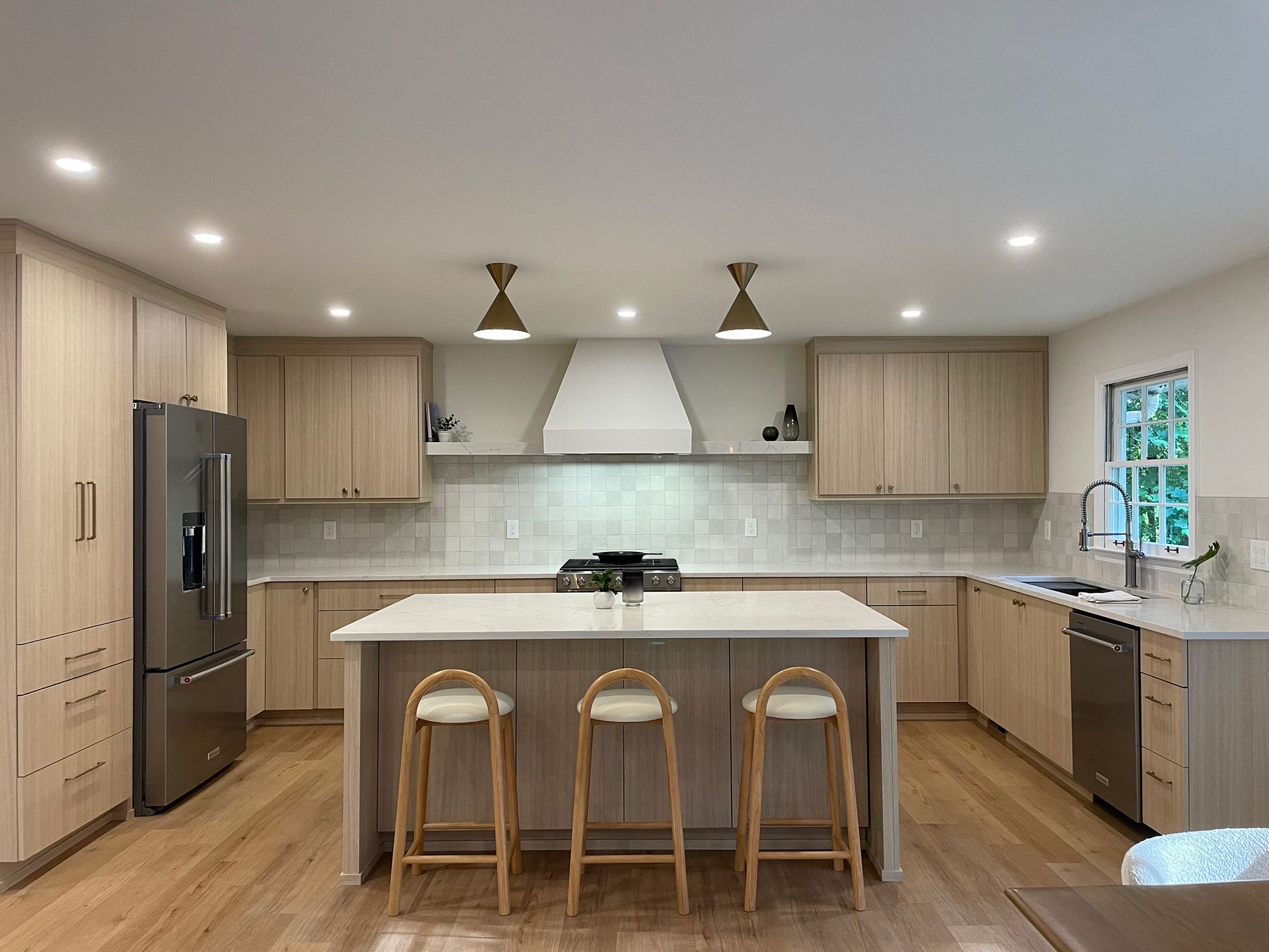 Modern kitchen with light wood cabinets, stainless steel appliances, and an island with three stools.