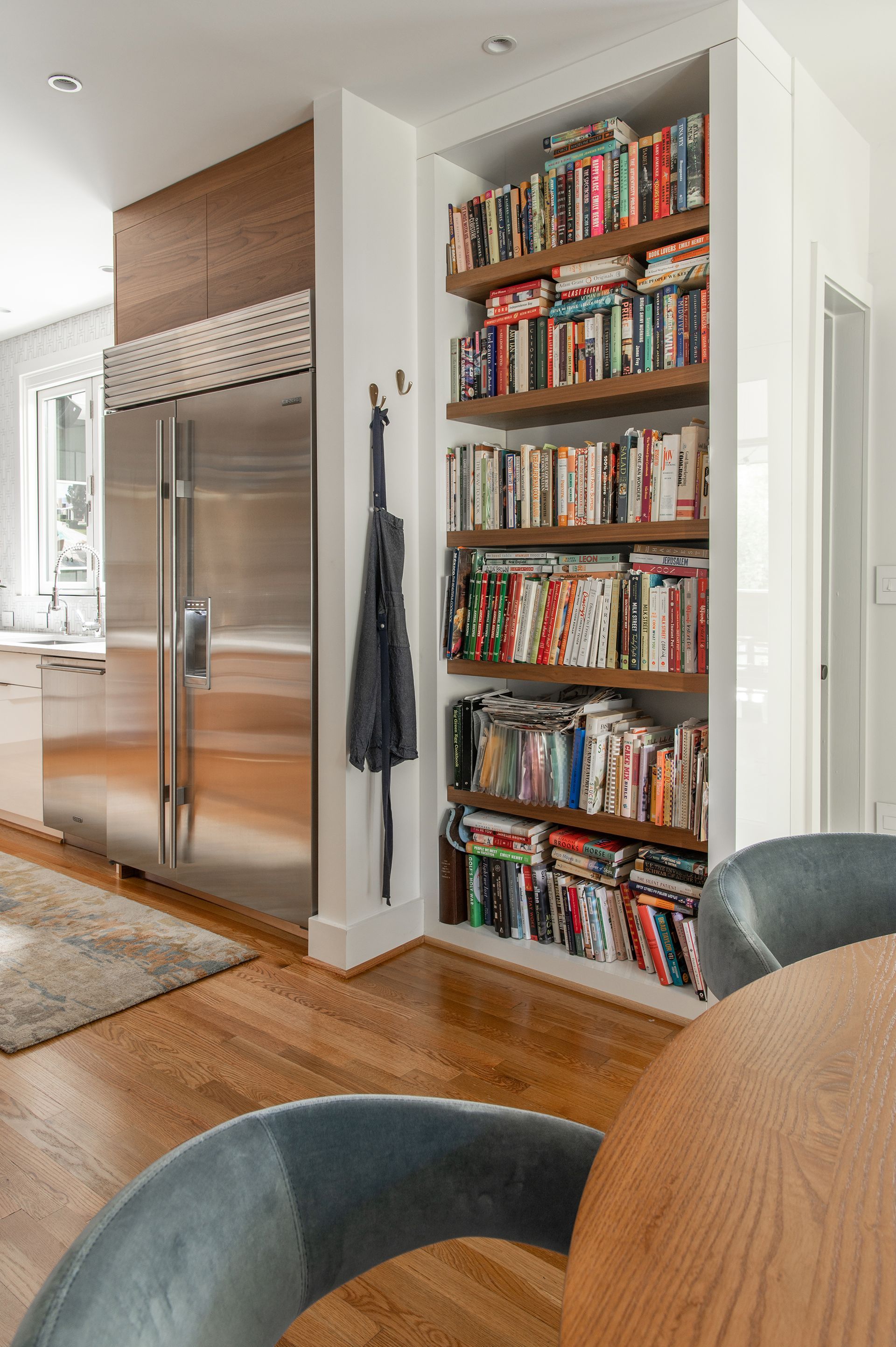 Bookshelves built into a kitchen wall, filled with books. Stainless steel refrigerator