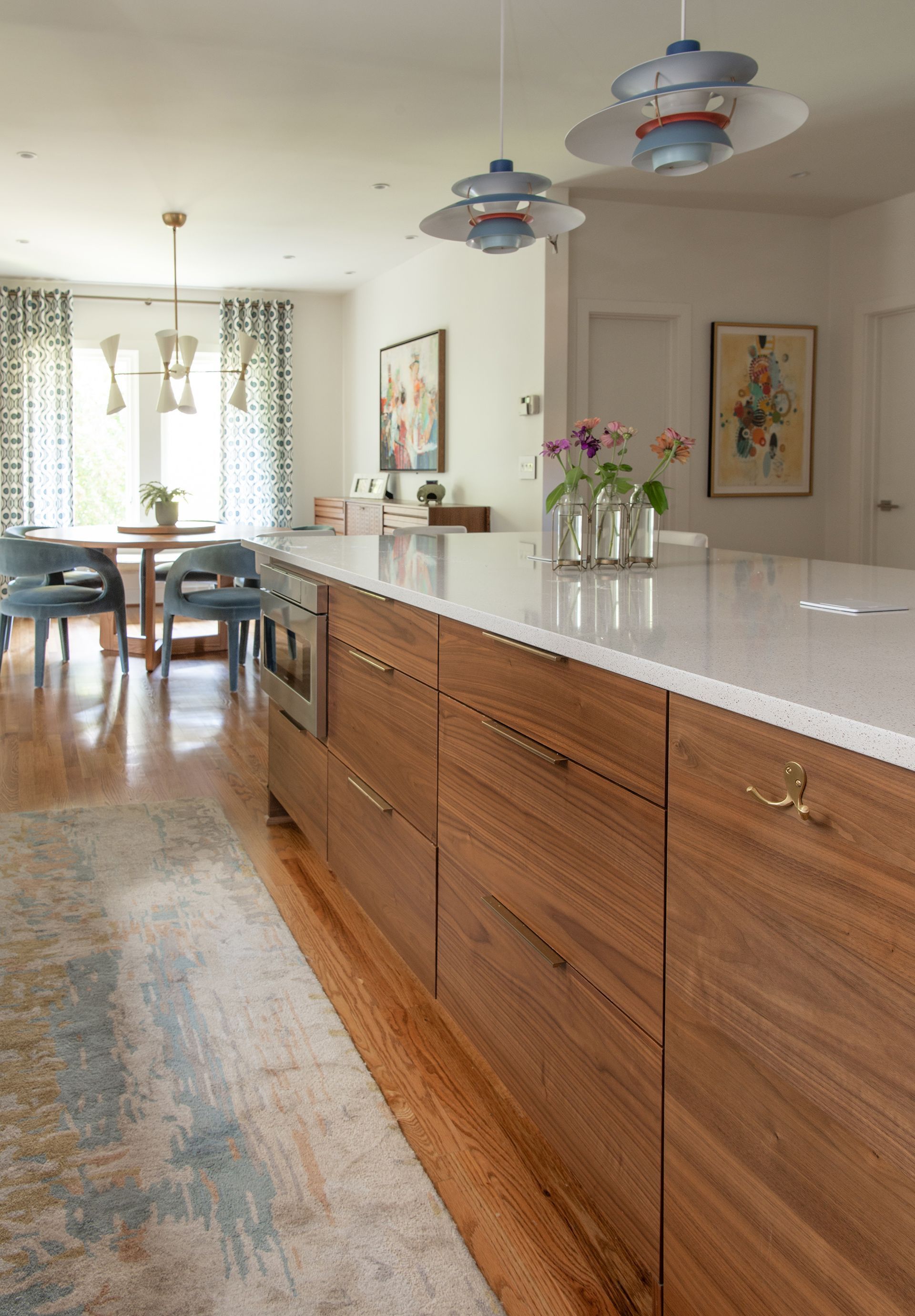Modern kitchen with wood cabinets, white countertop, and blue pendant lights.