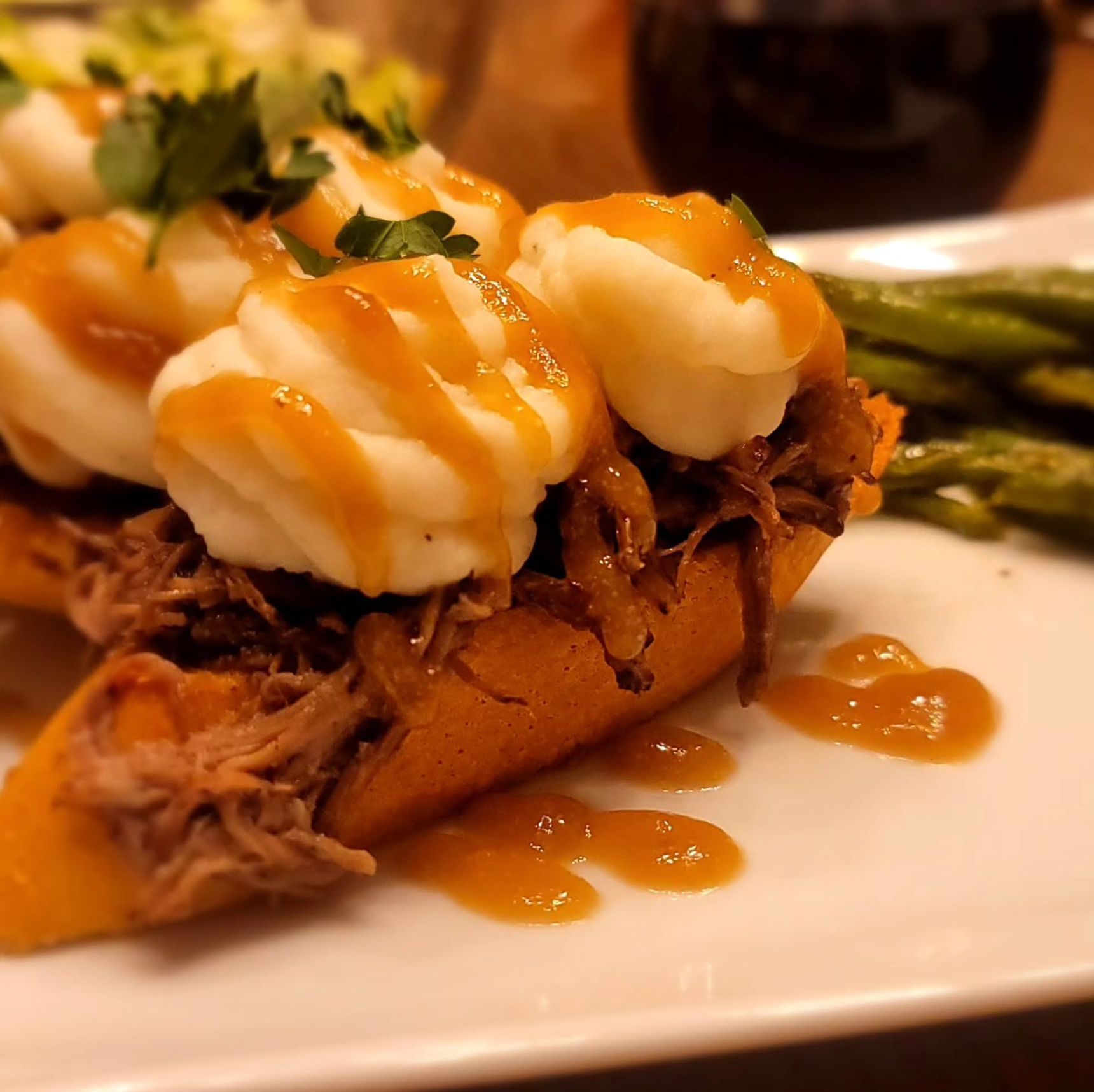 Pulled pork on a sweet potato topped with mashed potatoes and gravy, green beans on the side.