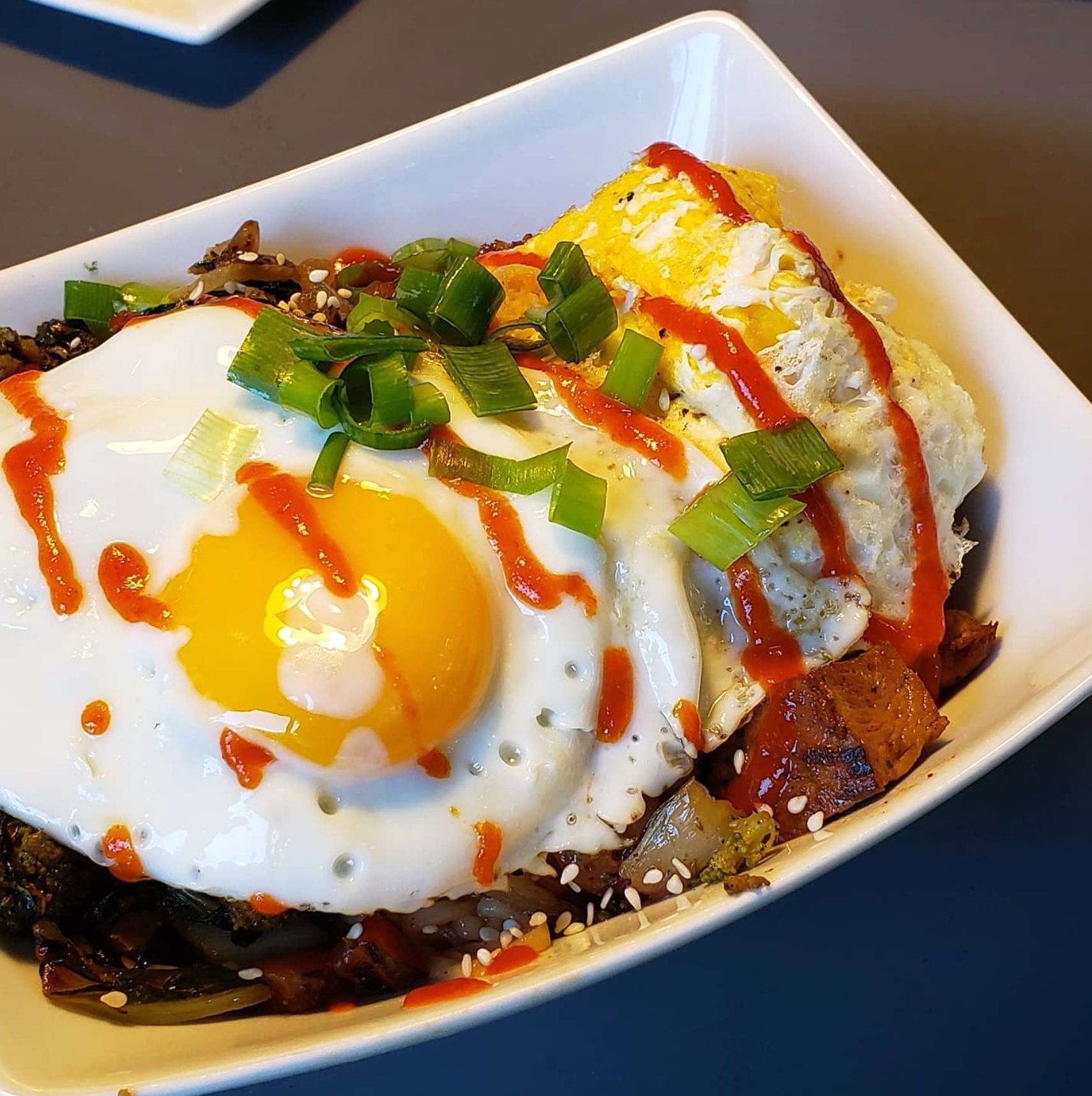 Bowl of food with fried eggs, sauce, and green onions.